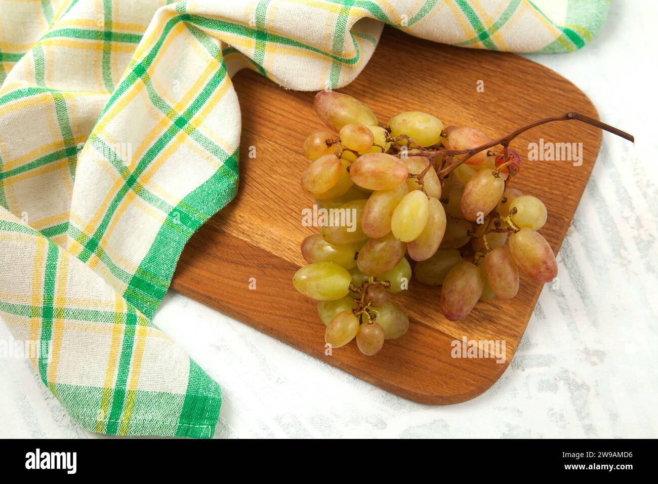 Schneidebrett mit einem großen Haufen reifer rosafarbener Trauben auf weiß. Rosafarbene Weintrauben mit blauem Küchentuch auf weißem hölzernem Hintergrund. Stockfoto