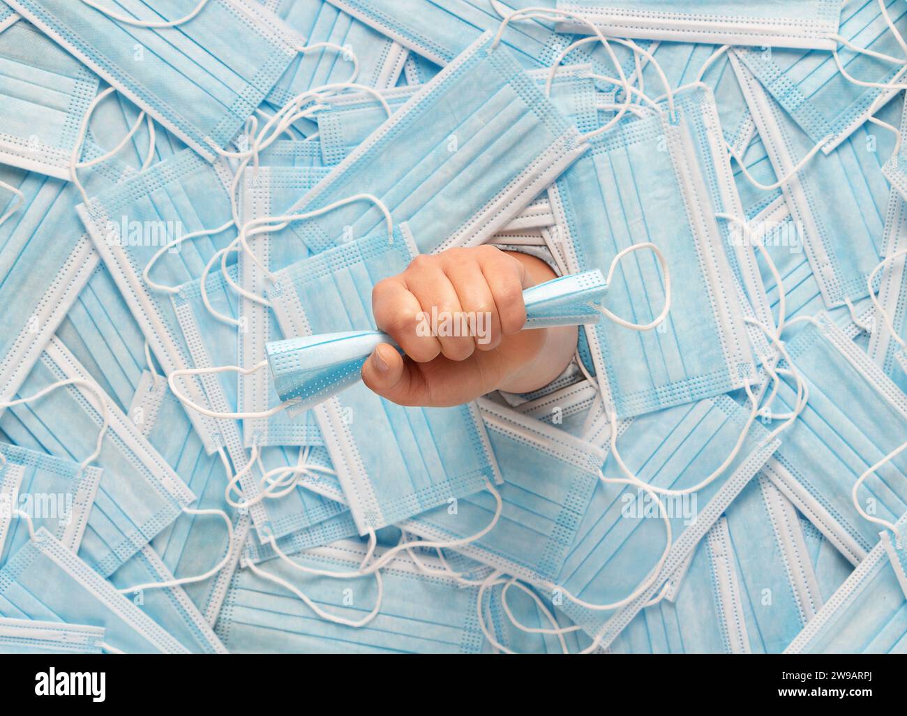 Medizinische Maske in einer weiblichen Hand vor dem Hintergrund einer großen Anzahl chirurgischer Masken. Draufsicht. Coronavirus-Pandemiekonzept. Stockfoto