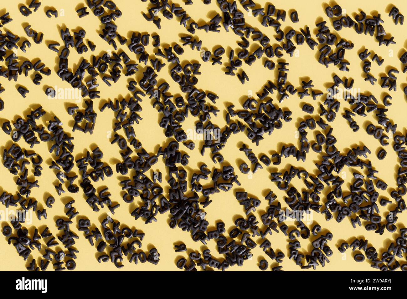 Gelber Hintergrund mit einer Vielzahl schwarzer Buchstaben, die über die Oberfläche verteilt sind, mit direktem Licht, das Schatten der Buchstaben erzeugt. Grafikressourcen Stockfoto