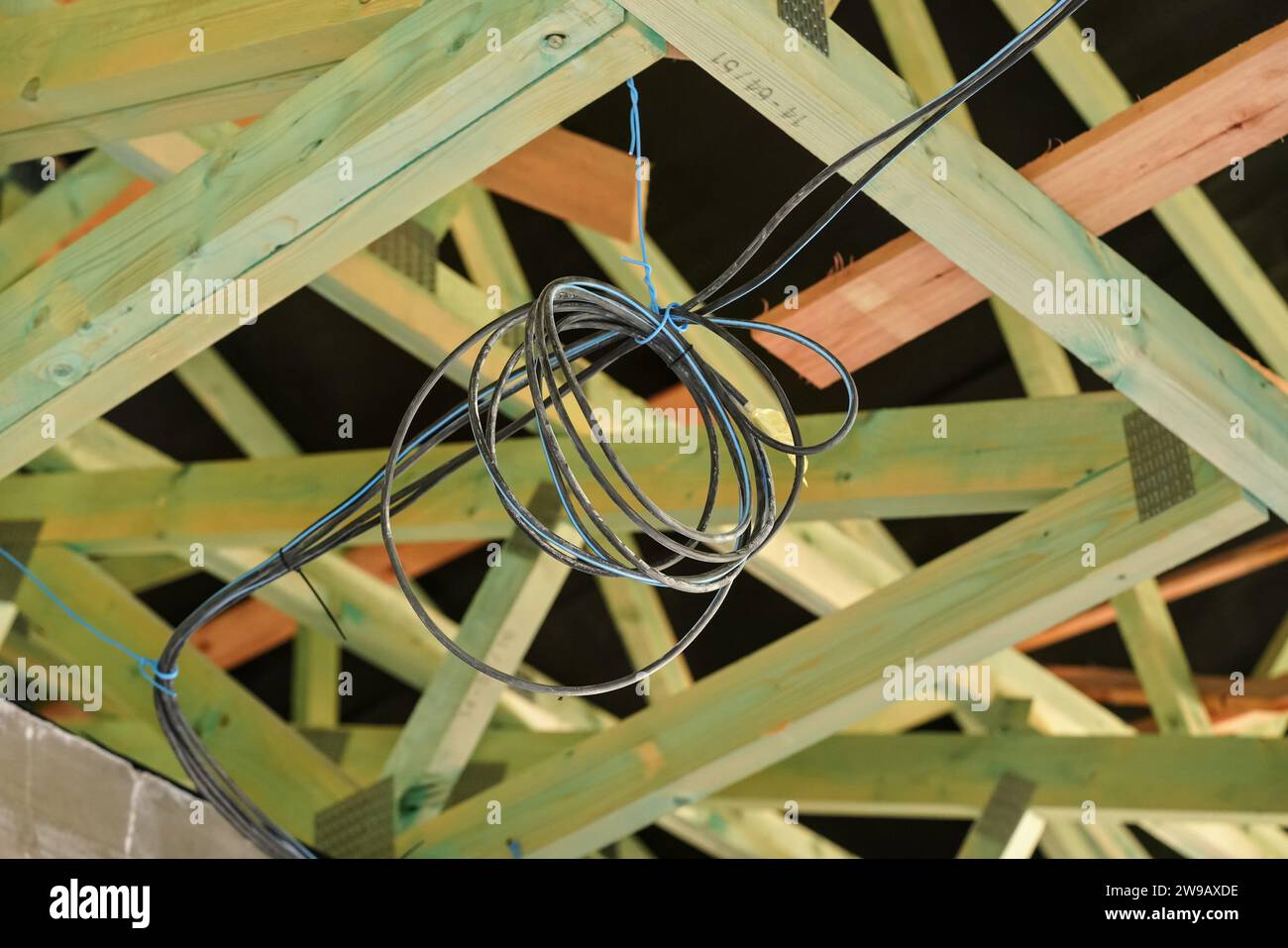 Holzbalken auf dem Dach der Neubaustelle, schwarze Elektrokabel hängen. Stockfoto