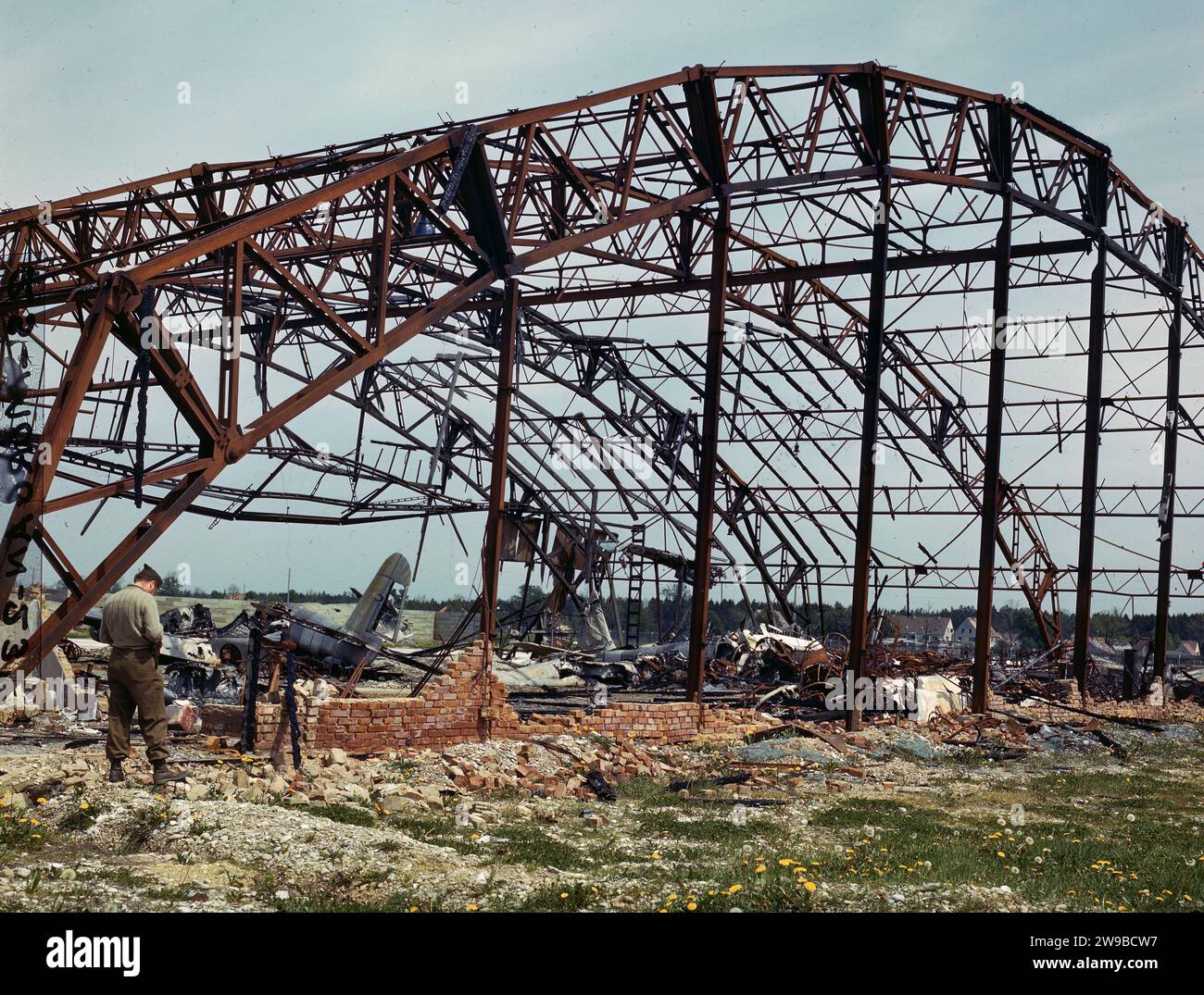 Die ME-410 liegt verbrannt und zerrissen in einem zerstörten Hangar der Messerschmitt Flugzeugfabrik in Augsburg. Ein US-amerikanischer Beobachter stellt den Schaden fest, den die alliierten Bombenangriffe 1945 angerichtet haben Stockfoto