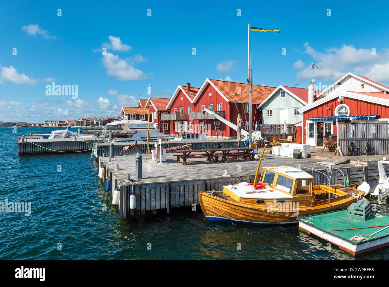 Lagerhäuser mit typischen roten Holzfassaden und Fischerbooten im Hafen von Skärhamn auf dem Archipel der Insel Tjörn im Sommer, Schweden Stockfoto