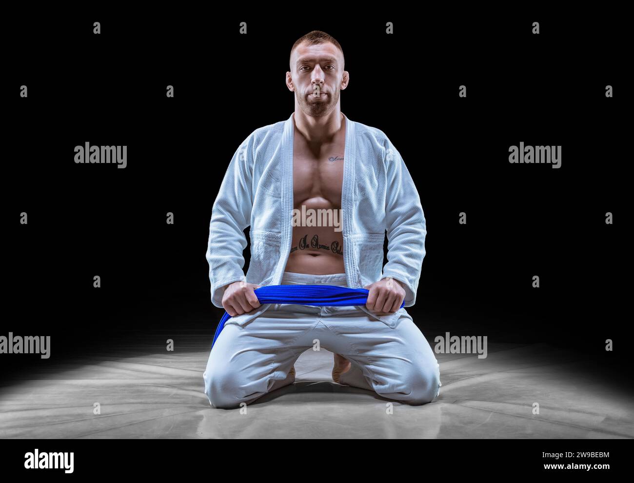 Profi-Athlet sitzt im Fitnessstudio in einem Kimono mit blauem Gürtel. Konzept von Karate, Jiu-Jitsu, Sambo, Judo. Gemischte Medien Stockfoto