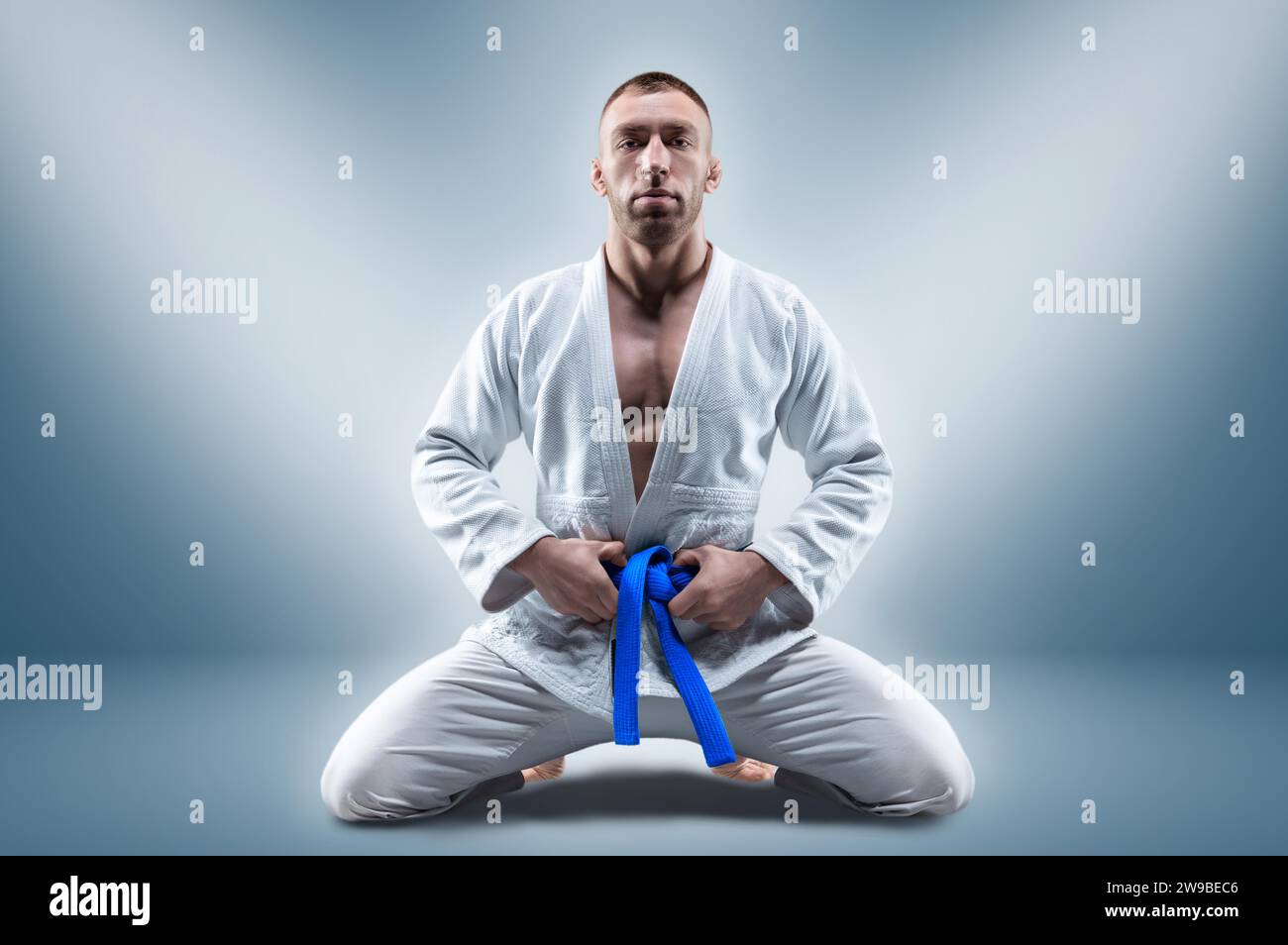 Athlet im Kimono mit blauem Gürtel sitzt und wartet auf den Gegner. Konzept von Karate, Sambo, Jujitsu. Gemischte Medien Stockfoto