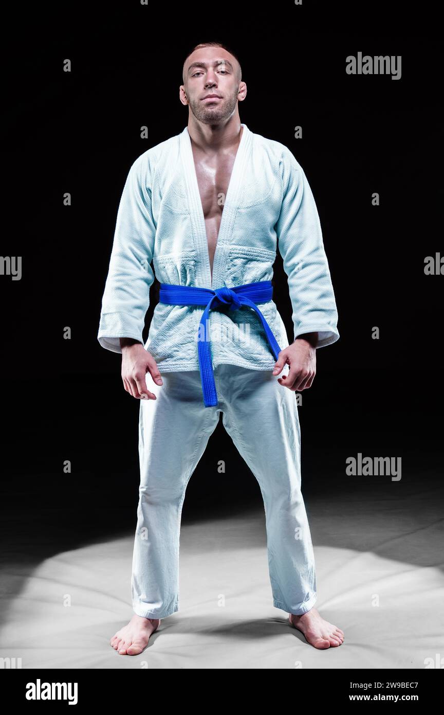 Profi-Athlet steht im Fitnessstudio in einem Kimono mit blauem Gürtel. Konzept von Karate, Jiu-Jitsu, Sambo, Judo. Gemischte Medien Stockfoto