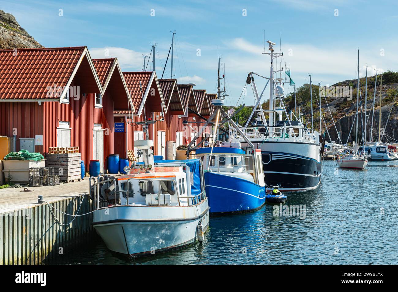 Lagerhäuser mit typischen roten Holzfassaden und Fischerbooten im Hafen von Skärhamn auf dem Archipel der Insel Tjörn im Sommer, Schweden Stockfoto