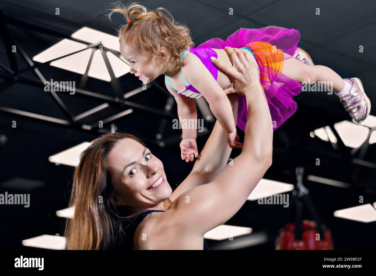 Mom wirft ihre Tochter ins Fitnessstudio. Gemischte Medien Stockfoto