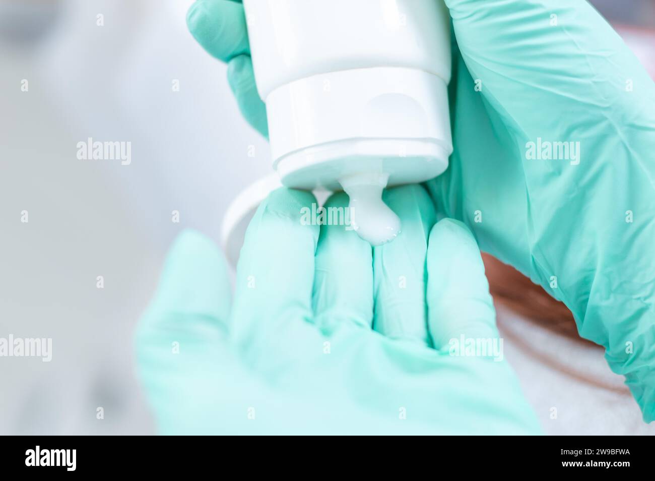 Bild von Händen in medizinischen Handschuhen, die Creme aus einem weißen Rohr drücken. Hautpflegekonzept. Gemischte Medien Stockfoto