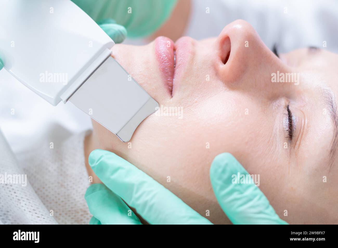 Junge hübsche Frau, die in Schönheitssalons behandelt wird. Ultraschallreinigungsverfahren. Hardware-Kosmetologie. Gemischte Medien Stockfoto