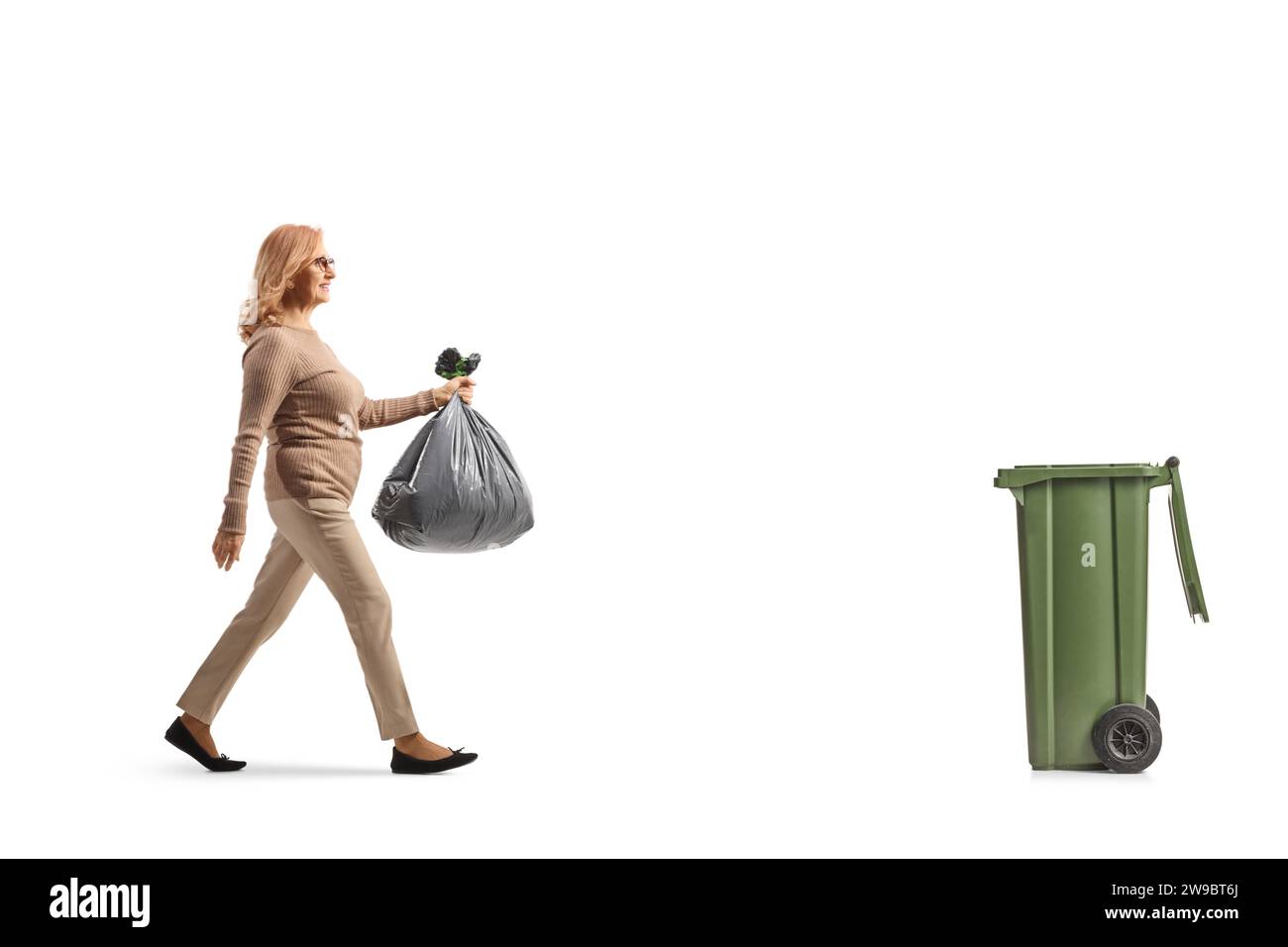 Profilaufnahme einer Frau mittleren Alters, die einen Plastikmüllbeutel trägt und zu einem Abfalleimer auf weißem Hintergrund geht Stockfoto