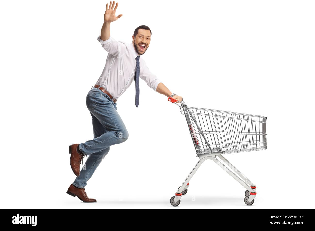 Fröhlicher Mann, der mit einem Einkaufswagen läuft und der Kamera zuwinkt, isoliert auf weißem Hintergrund Stockfoto