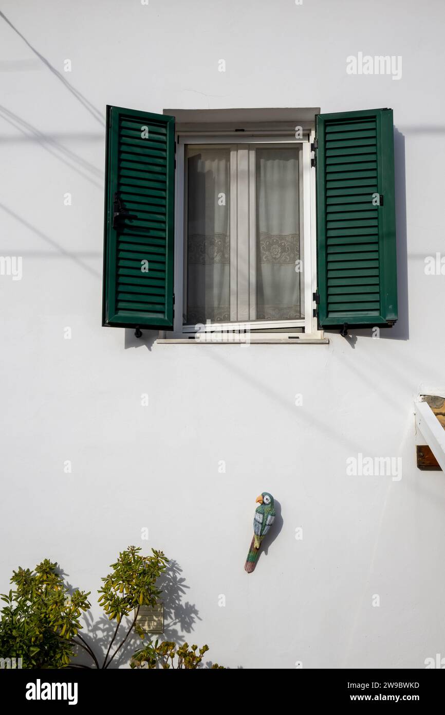 Detail des Weißen Hauses, in dem sich der lebende britische Schriftsteller Lawrence Durrell befand. Fenster mit grün geöffneten Rollläden. Holzpapagei schmückt die Wand. Kal Stockfoto