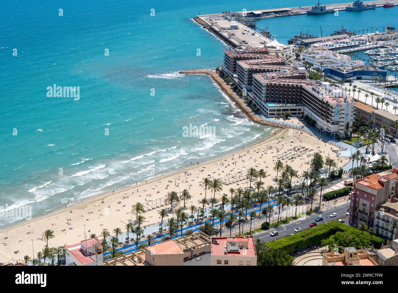 Strand mit Liegen und Schwimmen, auf dem Sand und im Meer, in der Nähe des Hafens von Alicante. Hochwertige Fotos Stockfoto
