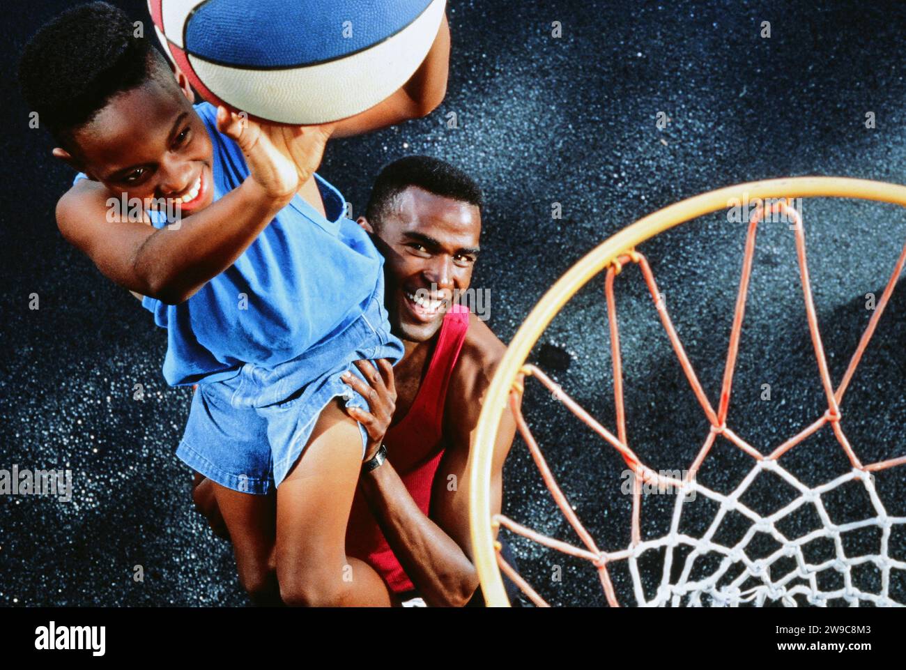 Ein afroamerikanischer Vater hebt seinen Sohn an, wie man einen Korb bei einem Basketballspiel gewinnt Stockfoto