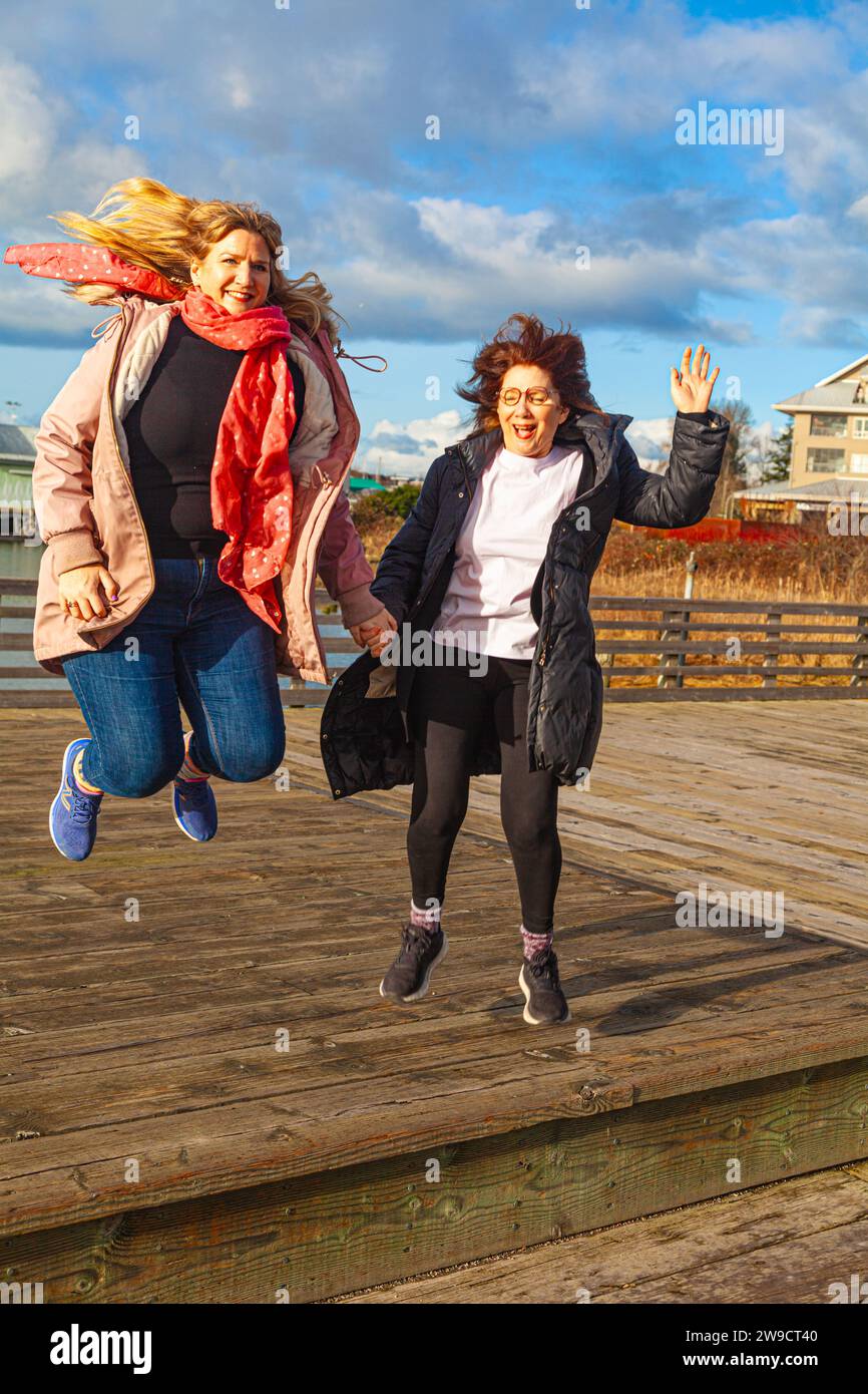 Mutter und Erwachsene Tochter springen vor Freude während der Weihnachtsfeiertage 2023 in Richmond, British Columbia, Kanada Stockfoto