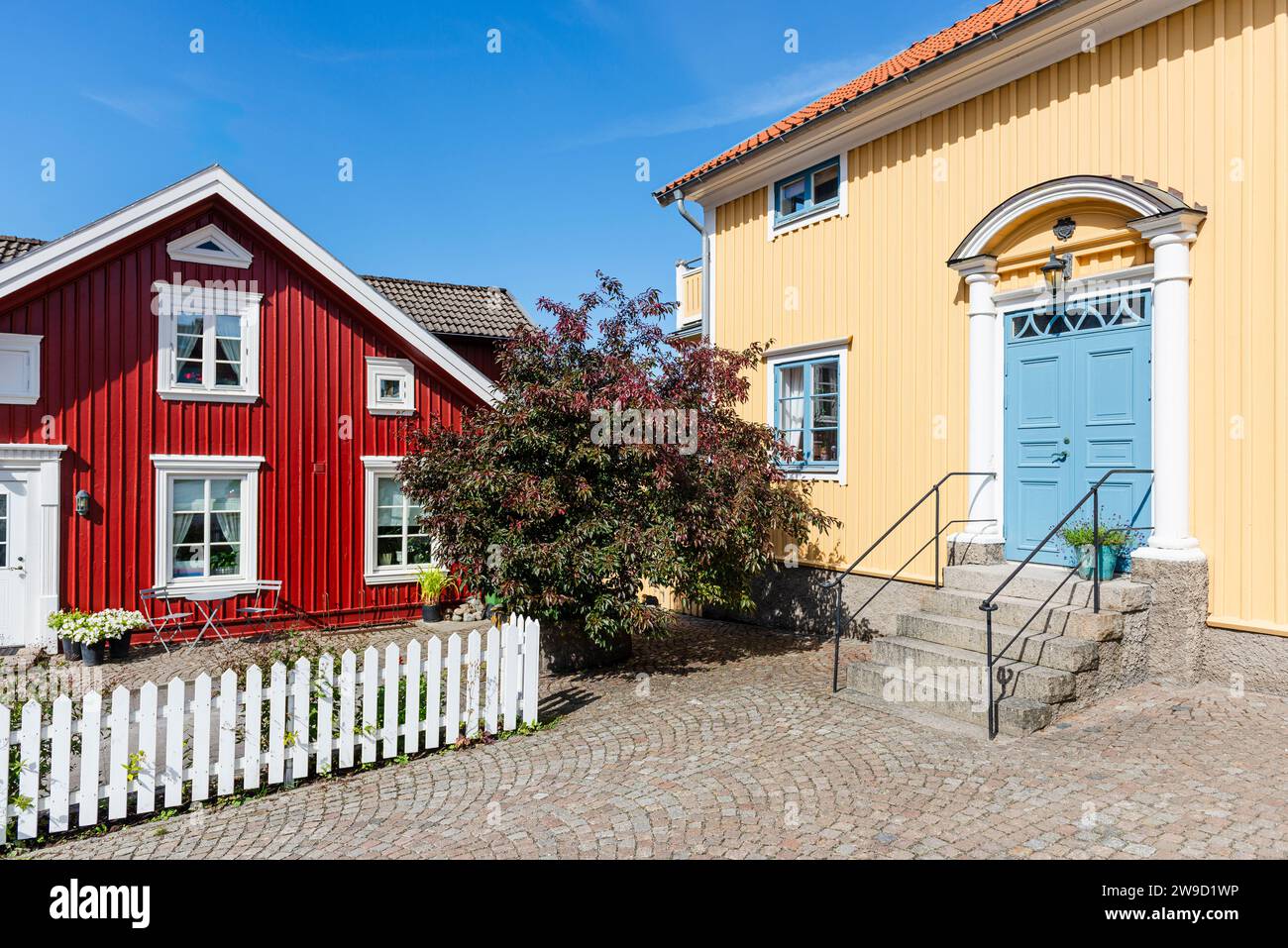 Eingangsportal mit blauer Tür auf einem gelben Holzhaus im Zentrum von Fjällbacka an der schwedischen Westküste bei Sonnenschein Stockfoto