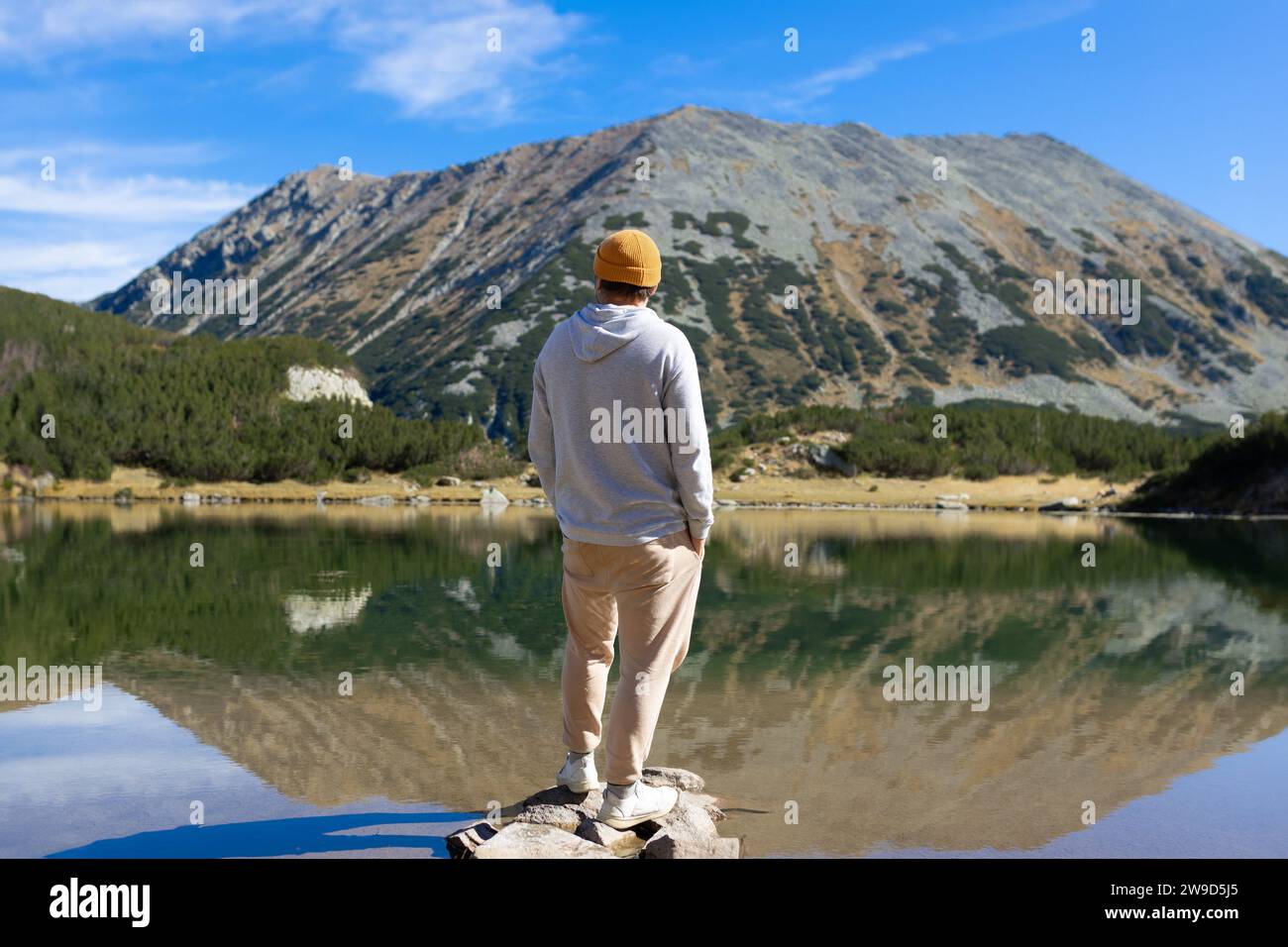 Junger Mann, der in der Nähe des Sees und der Berge steht und den Blick auf die Natur genießt Stockfoto