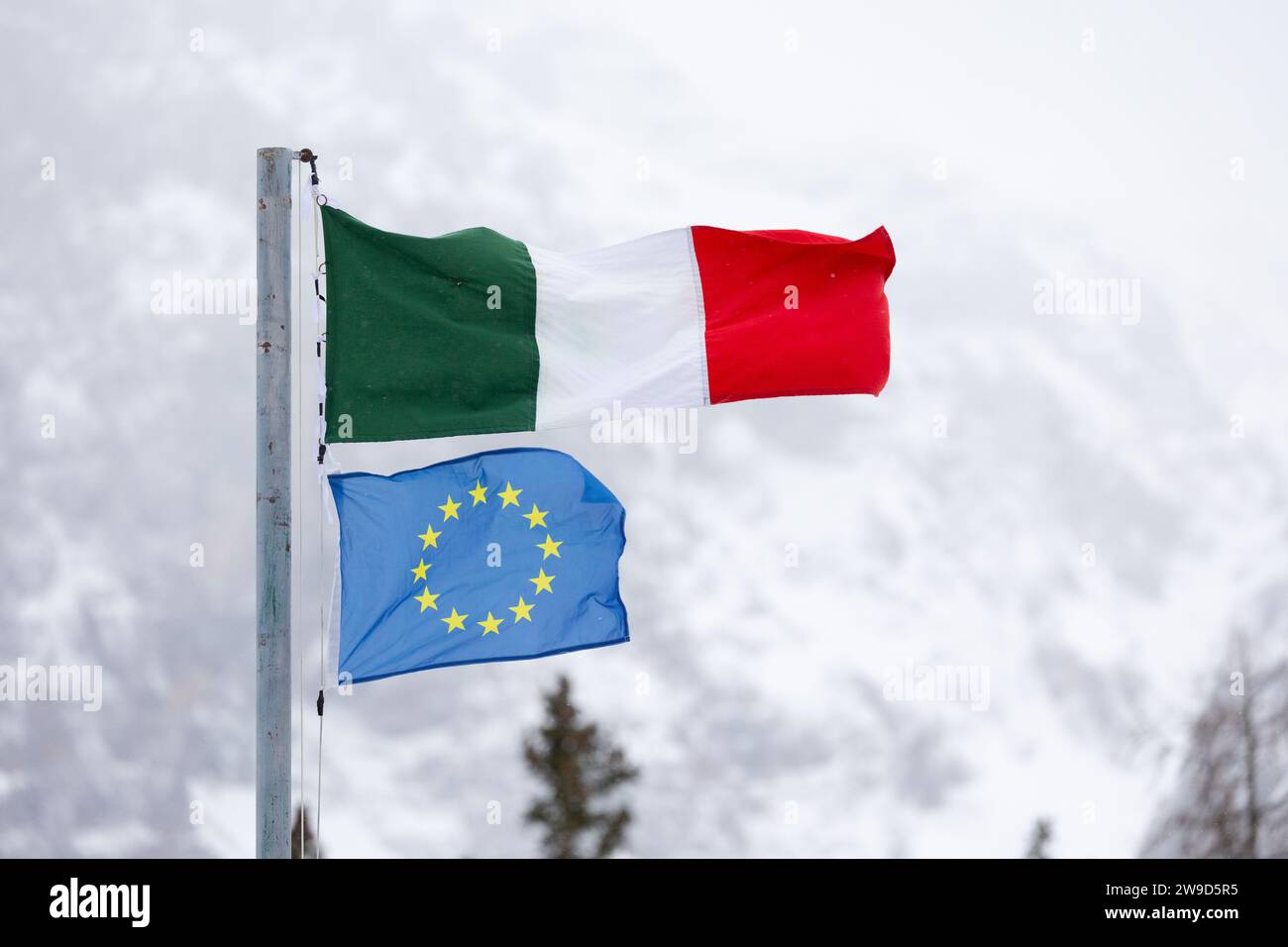 Die Fahnen Italiens und der EU (Europäische Union) fliegen zusammen vor dem Hintergrund der verschneiten italienischen Berge. Dolomiten im Winter. Stockfoto