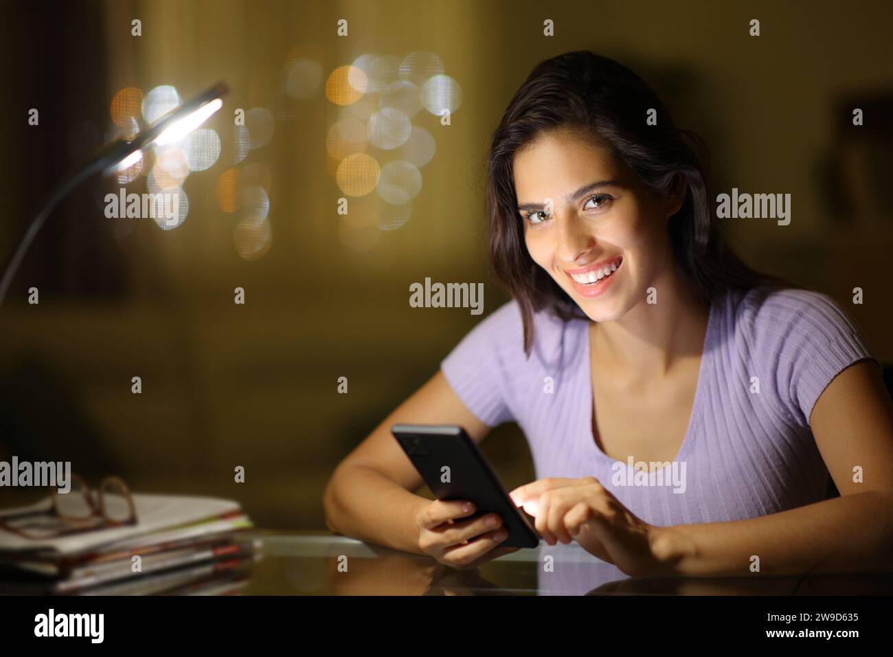 Eine glückliche Frau, die nachts das Telefon hält, sieht dich zu Hause an Stockfoto