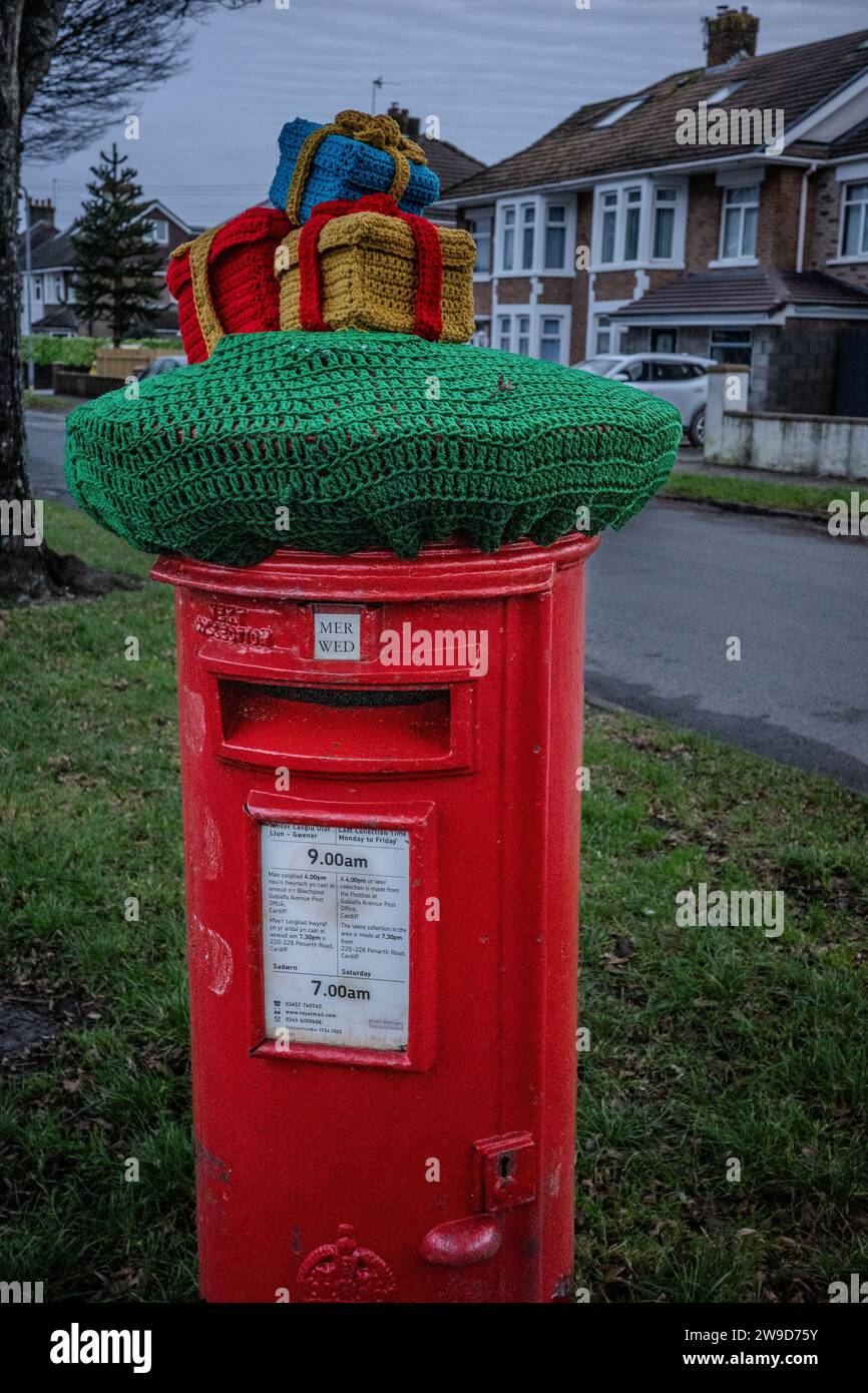 Dekorative gestrickte Geschenkboxen auf einem traditionellen roten britischen Briefkasten in einer Vorstadtstraße in Wales. Dezember 2023. Stockfoto