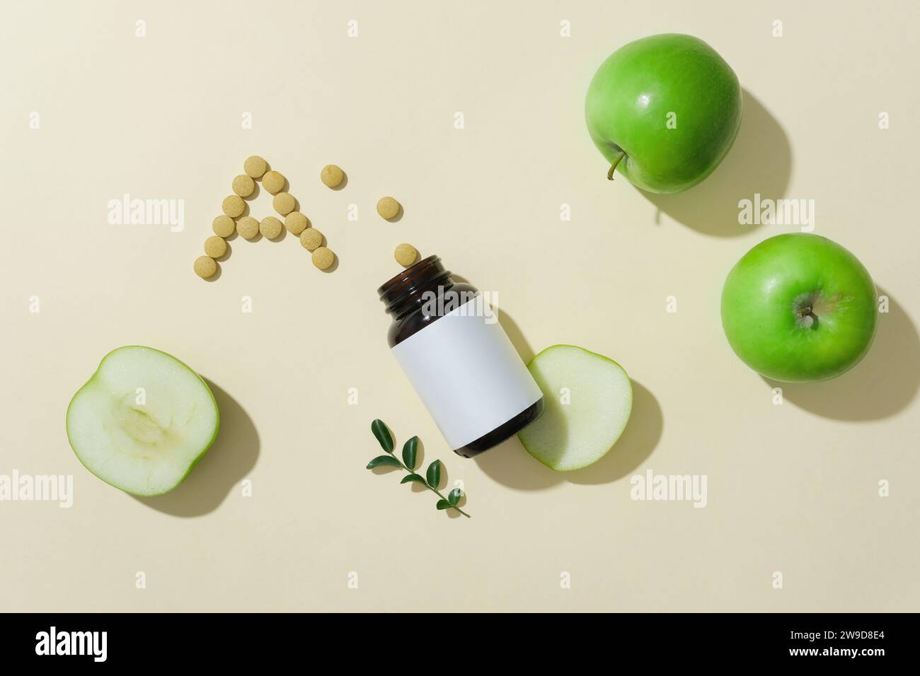 Eine bernsteinfarbene Flasche mit weißem Etikett, verziert mit grünen Äpfeln und Pillen in A-Form. Grüne Äpfel enthalten viel Vitamin A, das hilft Stockfoto