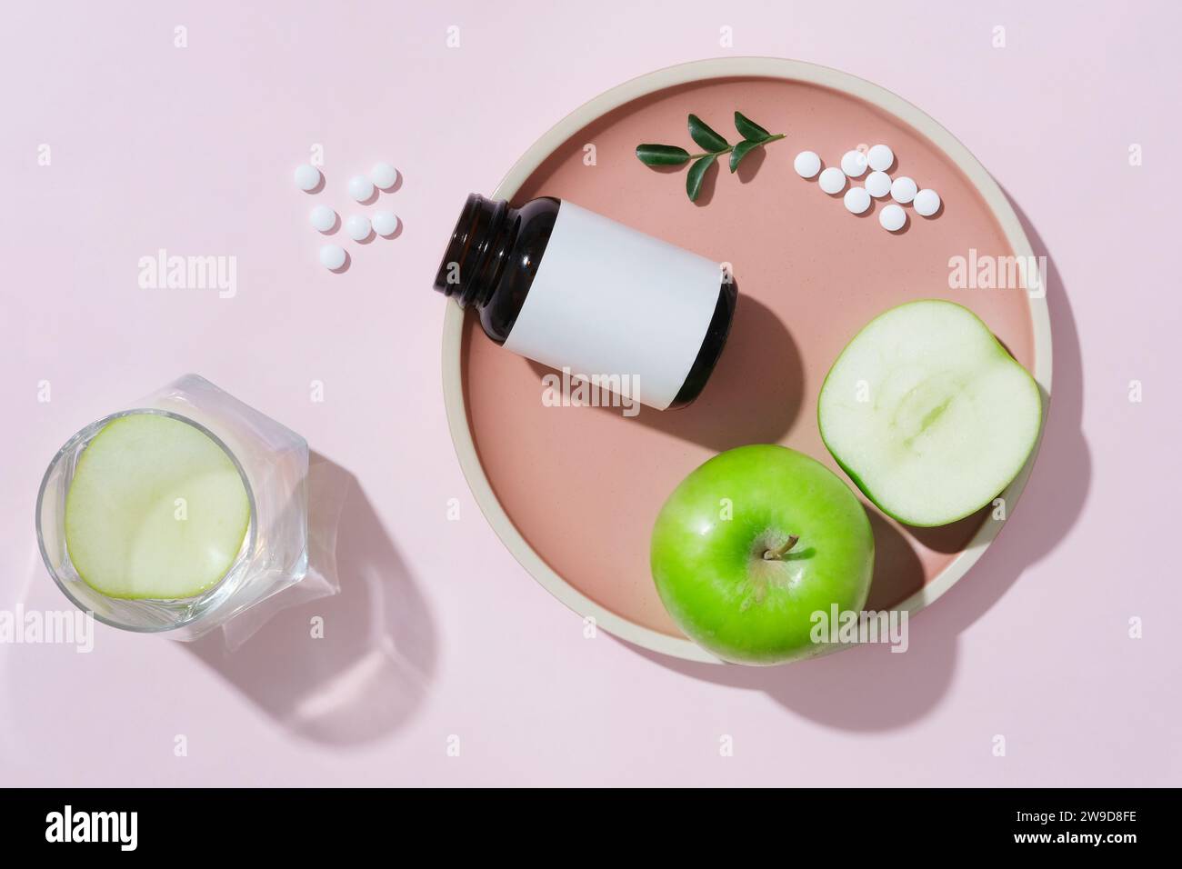 Auf einem rosa Keramikgeschirr, unbeschriftete Flasche mit grünen Äpfeln dekoriert. Konzept für Werbemittel aus grünem Apfel, reich an Vitaminen, Stockfoto