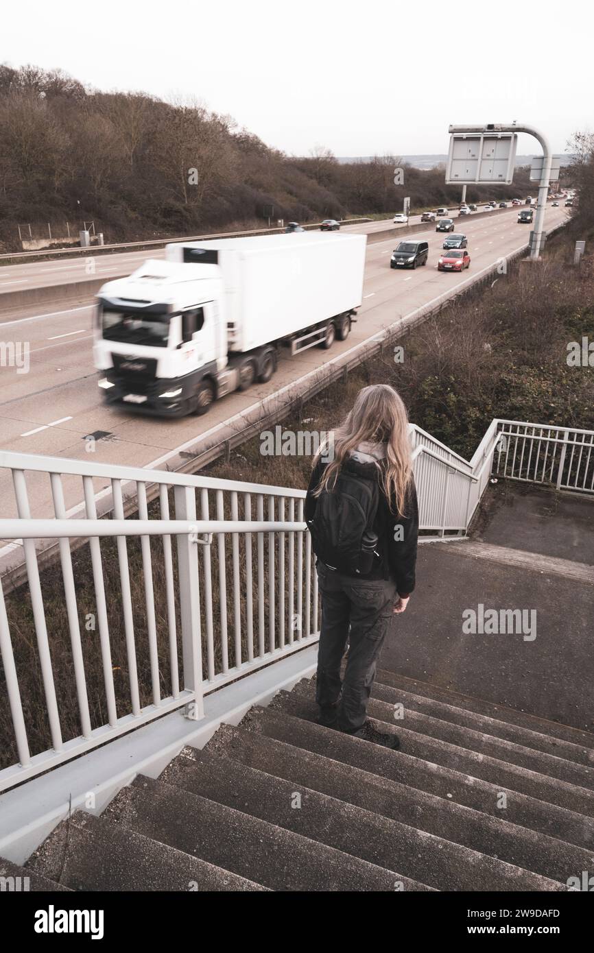 Eine Frau in einem kleinen Rucksack beobachtet den Verkehr auf der M25 von einer Treppe auf einer Fußgängerbrücke im Norden Londons, England Stockfoto