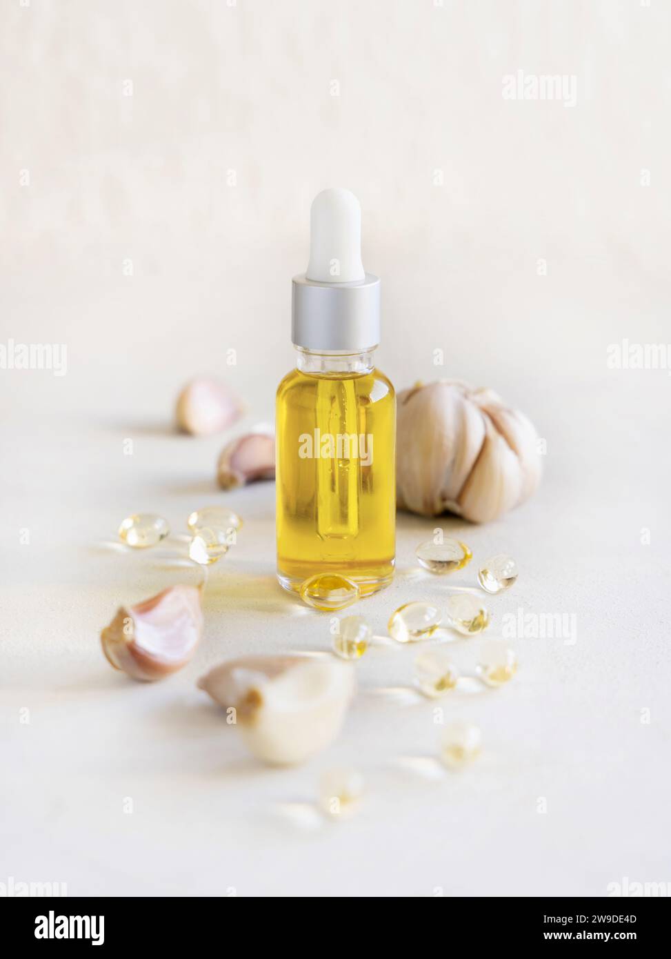 Knoblauchöl in einer Tropfflasche und Kapseln in der Nähe der ganzen Birne und Nelken auf einem weißen Tisch Nahaufnahme. Nahrungsergänzungsmittel mit antiviralen Eigenschaften, gut f Stockfoto
