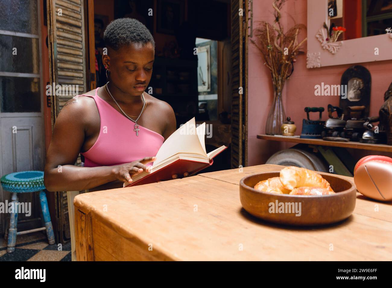 Junge haitianische Frau mit kurzen Haaren zu Hause sitzend bequem im Wohnzimmer, mit Croissants auf brauner Keramikplatte auf Tisch, lifestyl Stockfoto