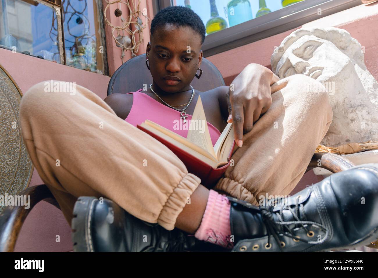 Nahaufnahme einer jungen, bequemen haitianischen Frau, die im Kreuz im hölzernen Schaukelstuhl sitzt und zu Hause studiert und ein großes Buch hält. Stockfoto