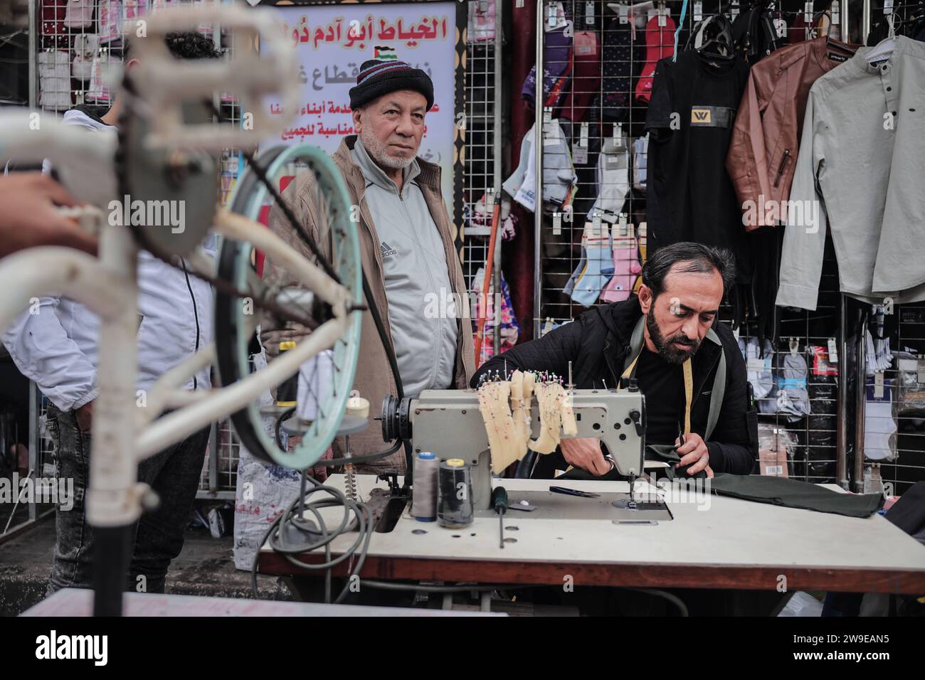 Ein palästinensischer Schneider namens Abu Adam Dolah verwendet eine Nähmaschine mit Pedalbedienung, die er aufgrund von Stromknappheit entwickelt Hat Ein palästinensischer Schneider namens Abu Adam Dolah verwendet eine Nähmaschine mit Pedalbedienung, die er aufgrund von Stromknappheit entwickelt hat, da Israel am 27. Dezember 2023 in Rafah, Gaza, die Macht blockiert. Gashda befestigte Fahrradpedale an seiner Nähmaschine so, dass er die Maschine ohne Strom benutzen konnte. Foto: Bashar Taleb apaimages Rafah Gazastreifen palästinensisches Gebiet 271223_Rafah_BT_0010 Copyright: XapaimagesxBasharxTalebxapaimagesx Stockfoto