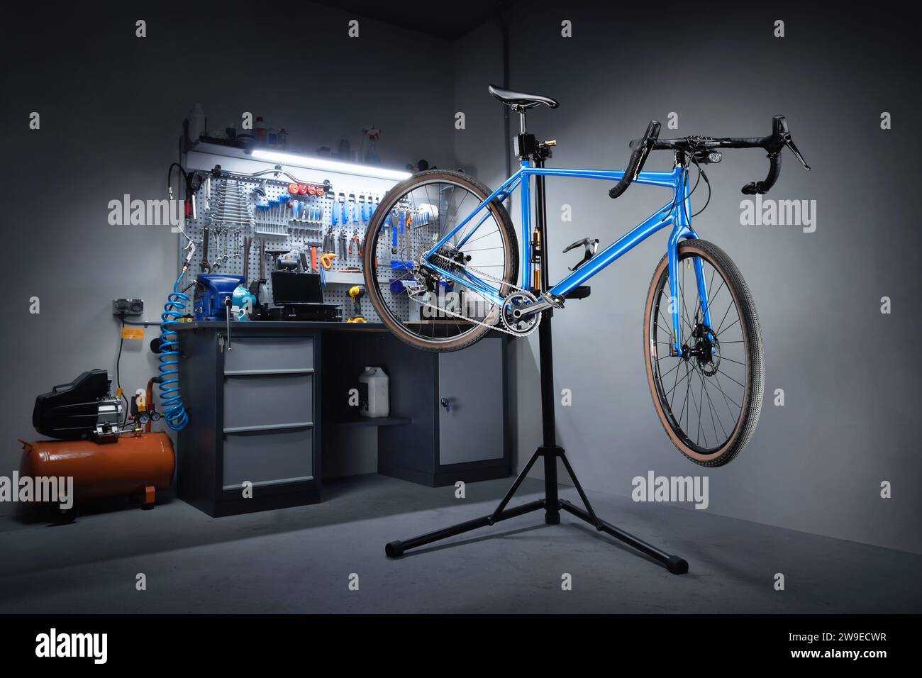 Fahrradwerkstatt zur Reparatur von Fahrrädern. Fahrrad hängt an einem Reparaturständer im Hintergrund einer Werkbank mit professionellen Werkzeugen. Fahrradservice. Stockfoto