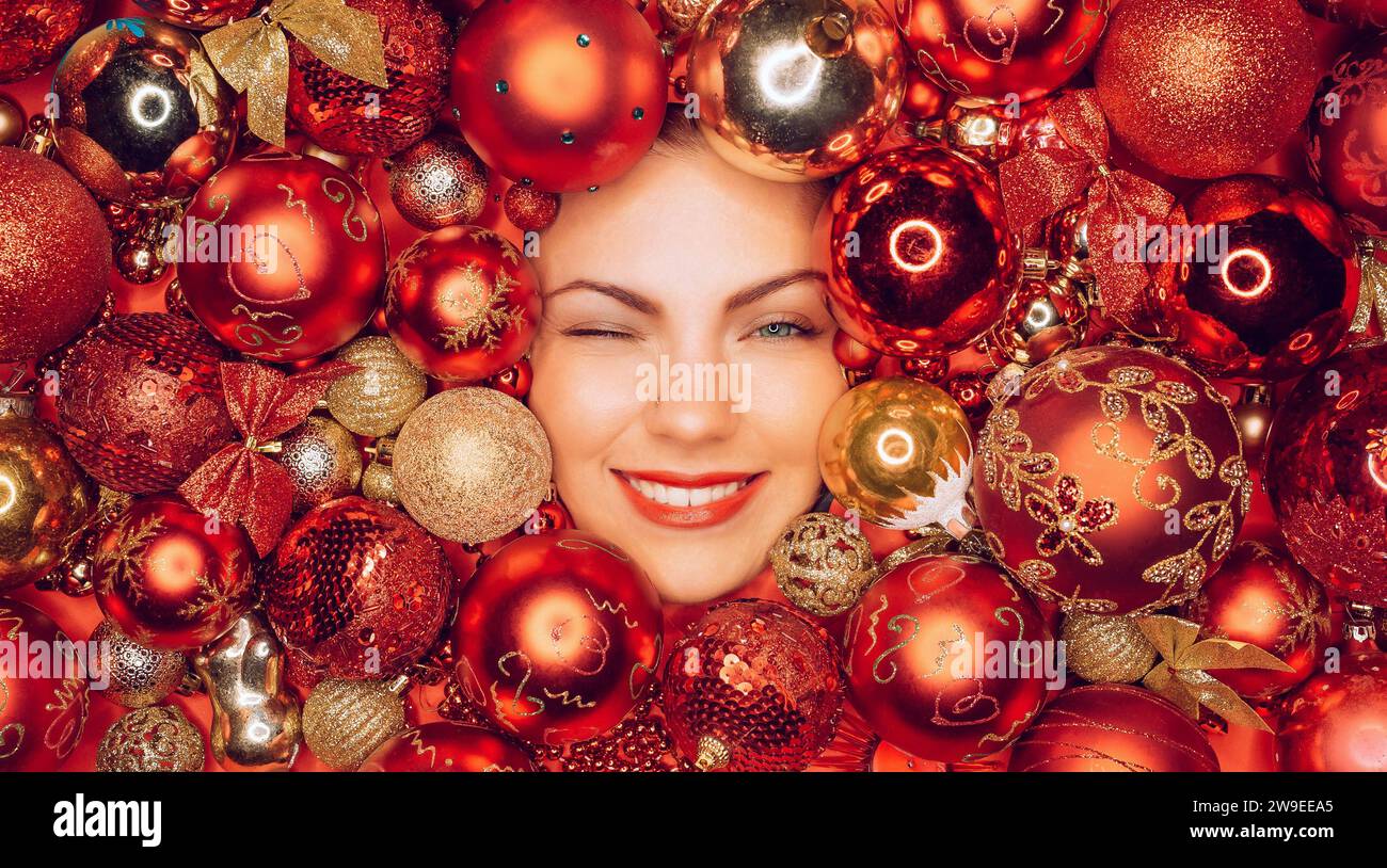 Glückliche Frau blinkte vor Freudenlächeln in roten Weihnachtsbaumkugeln. Feiertage. Stockfoto