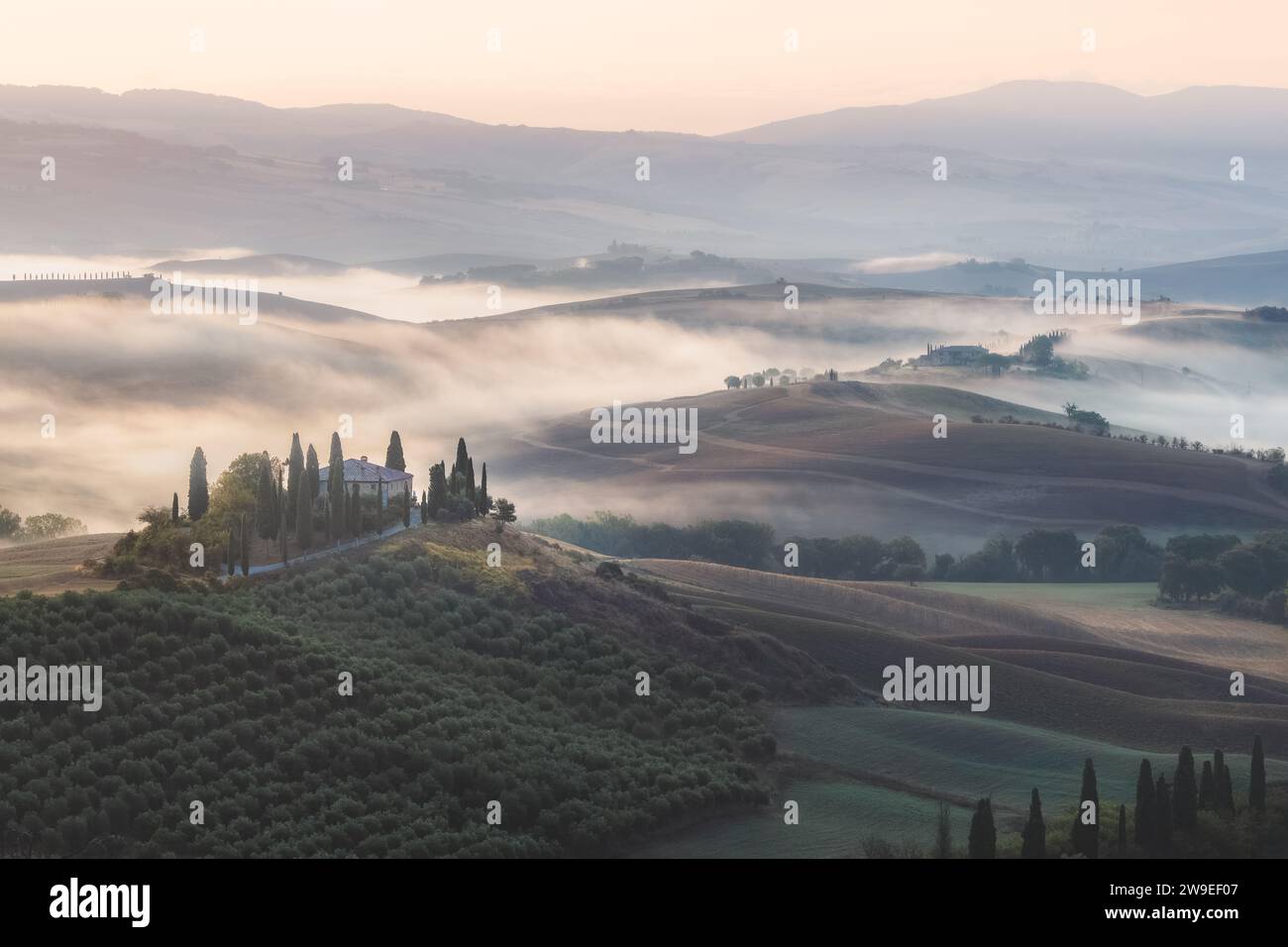 Stimmungsvoller Sonnenaufgang Nebel durch das Tal von Val d'Orcia und ein rustikales Bauernhaus in der malerischen Landschaft und sanften Hügeln der ländlichen Toskana Stockfoto