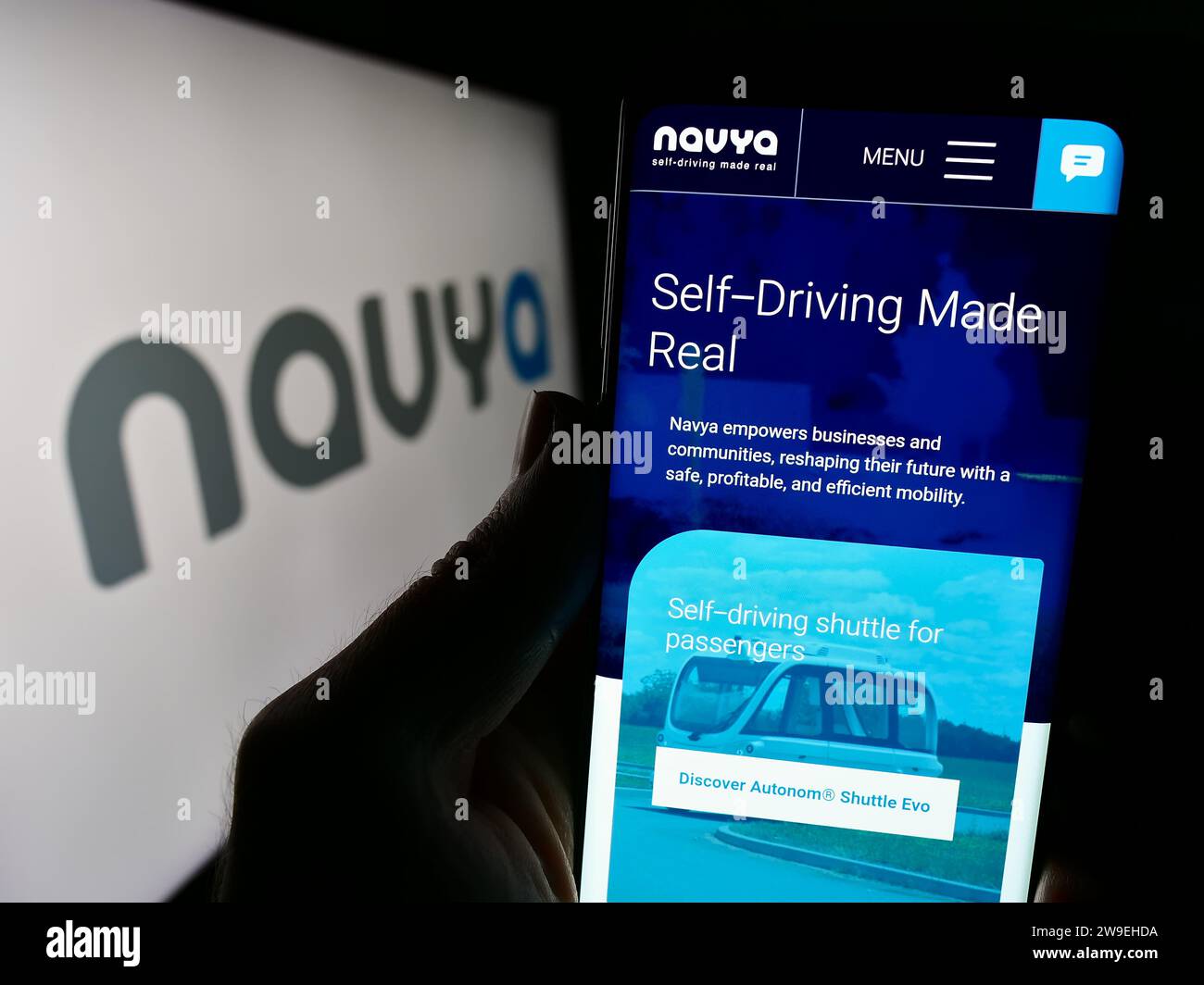 Person mit Smartphone und Website des französischen Autonome Fahrzeugunternehmens Navya S.A. vor dem Logo. Konzentrieren Sie sich auf die Mitte des Telefondisplays. Stockfoto