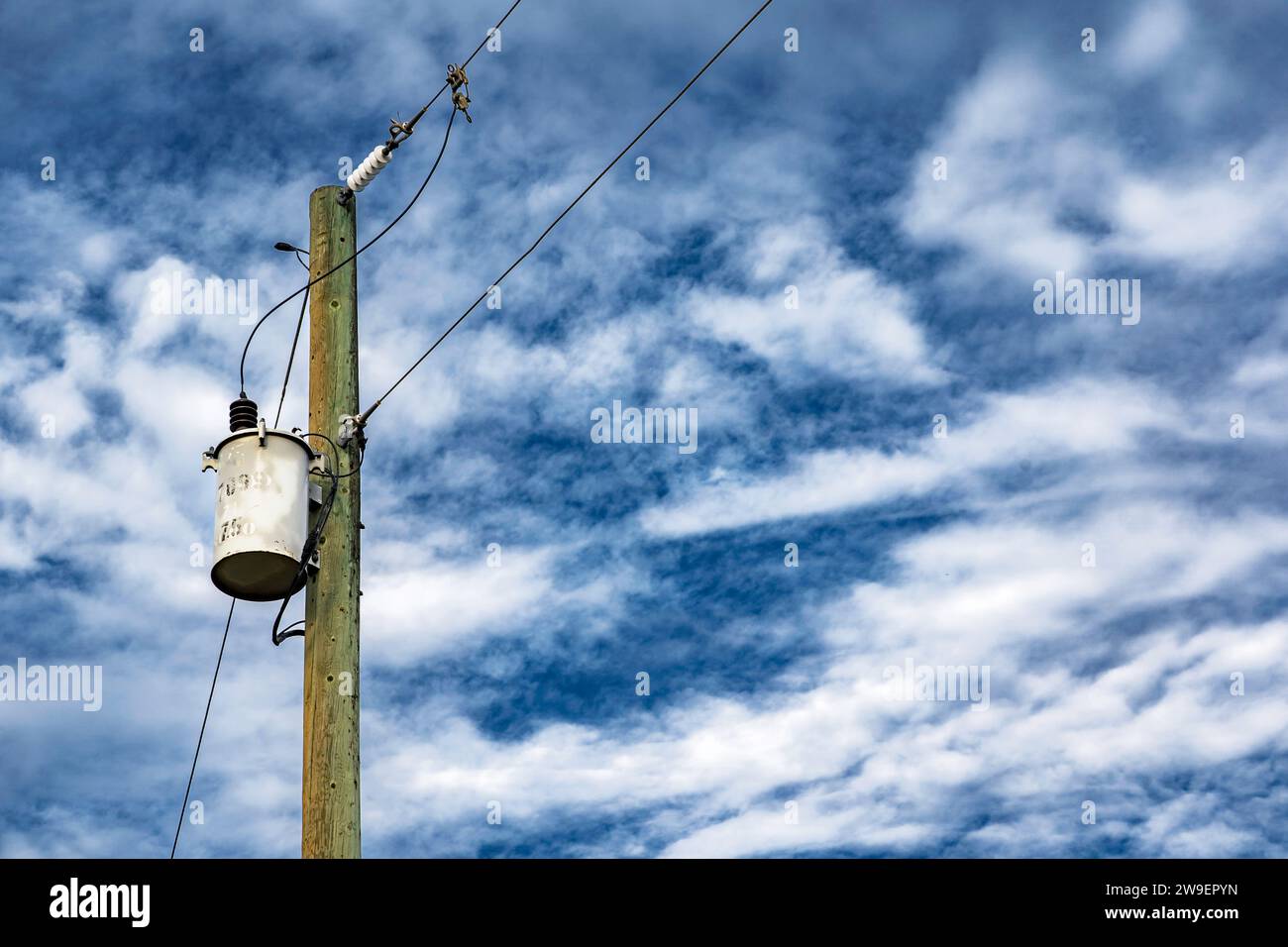 Hölzerne Strommasten mit Netzteilen und Stromleitungen vor einem blauen, bewölkten Himmel im ländlichen Alberta Kanada. Stockfoto