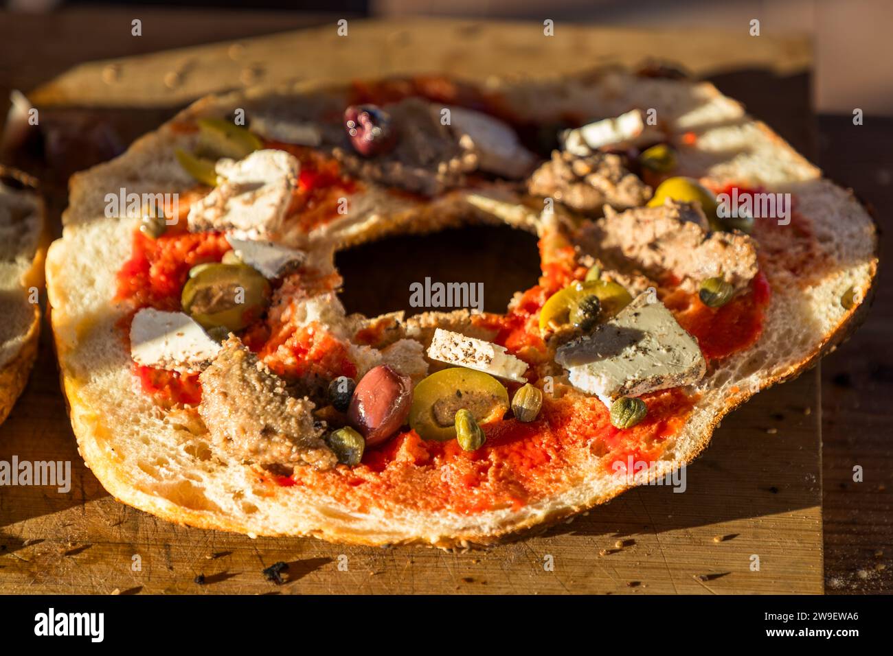 Ein vollständig belegtes ringförmiges Ftira-Fladenbrot mit Tomatensauce, ġbejna-Käse, Oliven, Kapern und Thunfisch ist bereit für den Holzofen im Girgenti Olive Grove in Siġġiewi, Malta, wo Besucher es selbst backen. Die traditionelle maltesische Ftira wurde 2020 in die UNESCO-Liste des immateriellen Kulturerbes aufgenommen. Stockfoto