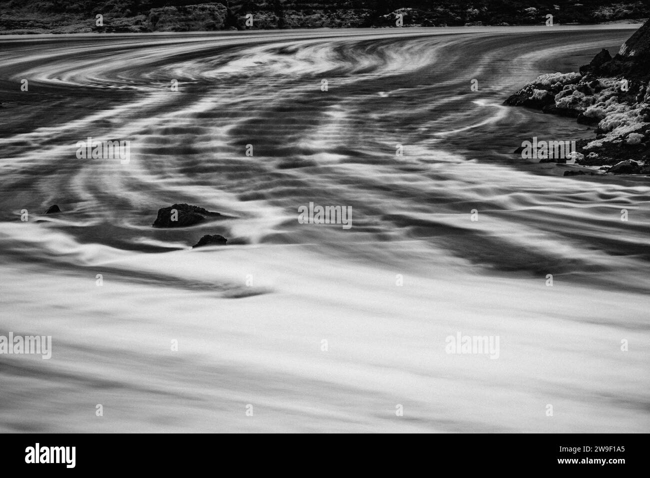 Das Wasser fließt über eine Damm-Struktur und stürzt auf den Boden des Überlaufs, wodurch Schaum entsteht und Spuren auf dem Wasser am Boden hinterlassen. Stockfoto