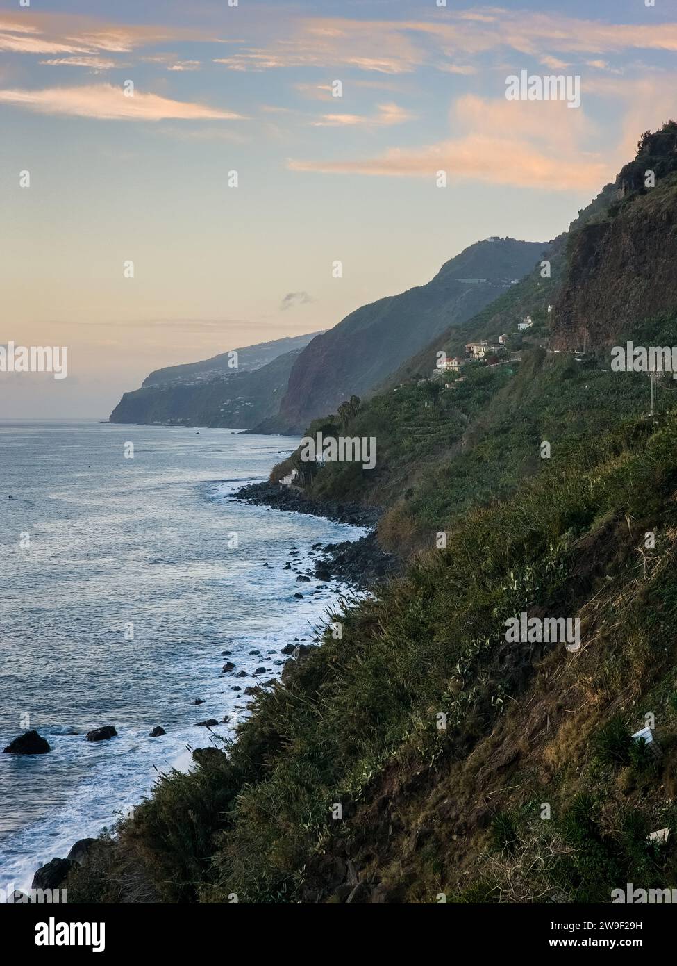 Ein reifer Erwachsener steht allein auf einem felsigen Berghang mit Blick auf den ruhigen Ozean Stockfoto