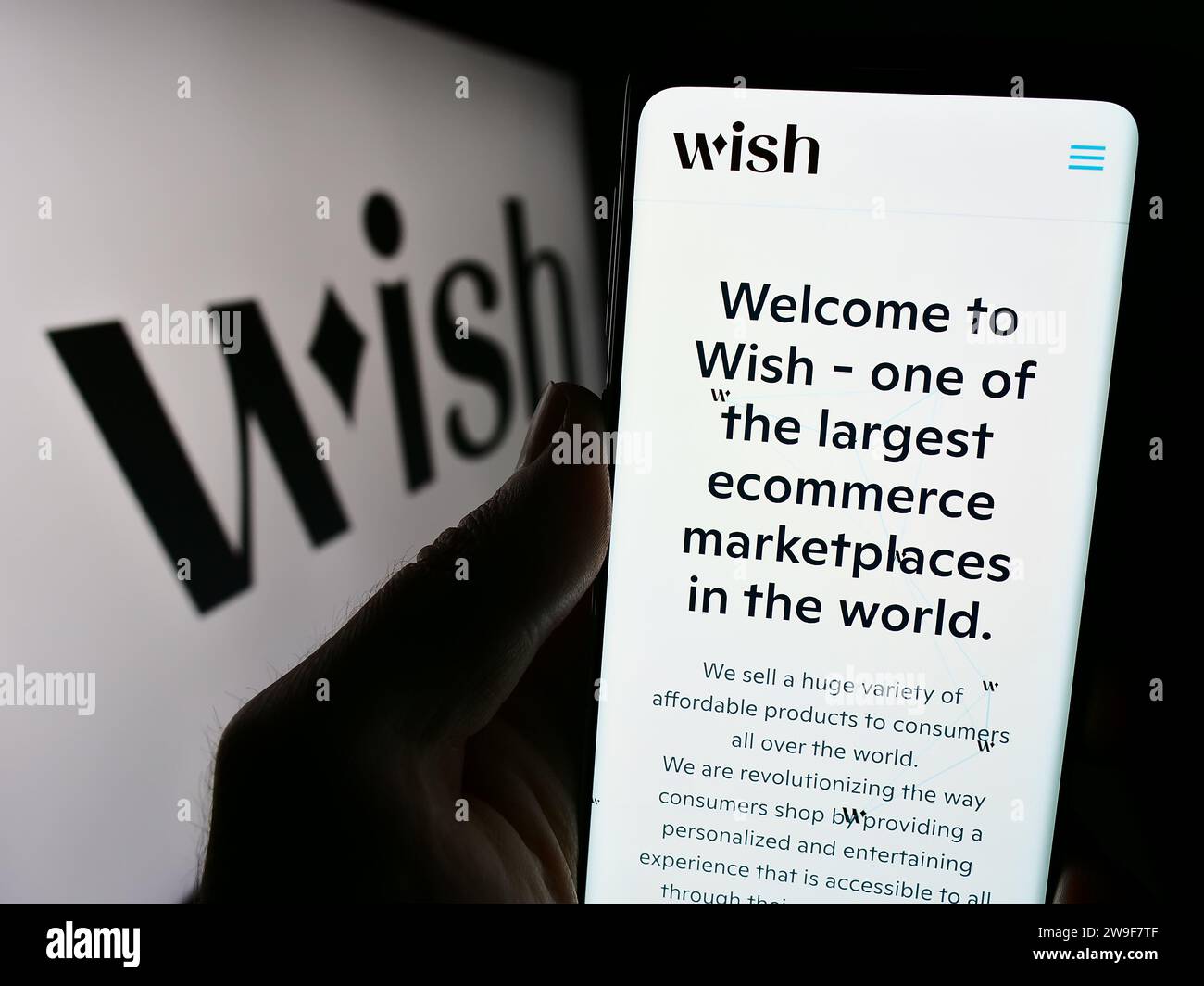 Person, die ein Mobiltelefon mit der Webseite des US-amerikanischen E-Commerce-Plattformunternehmens Wish.com vor dem Geschäftslogo hält. Konzentrieren Sie sich auf die Mitte des Telefondisplays. Stockfoto