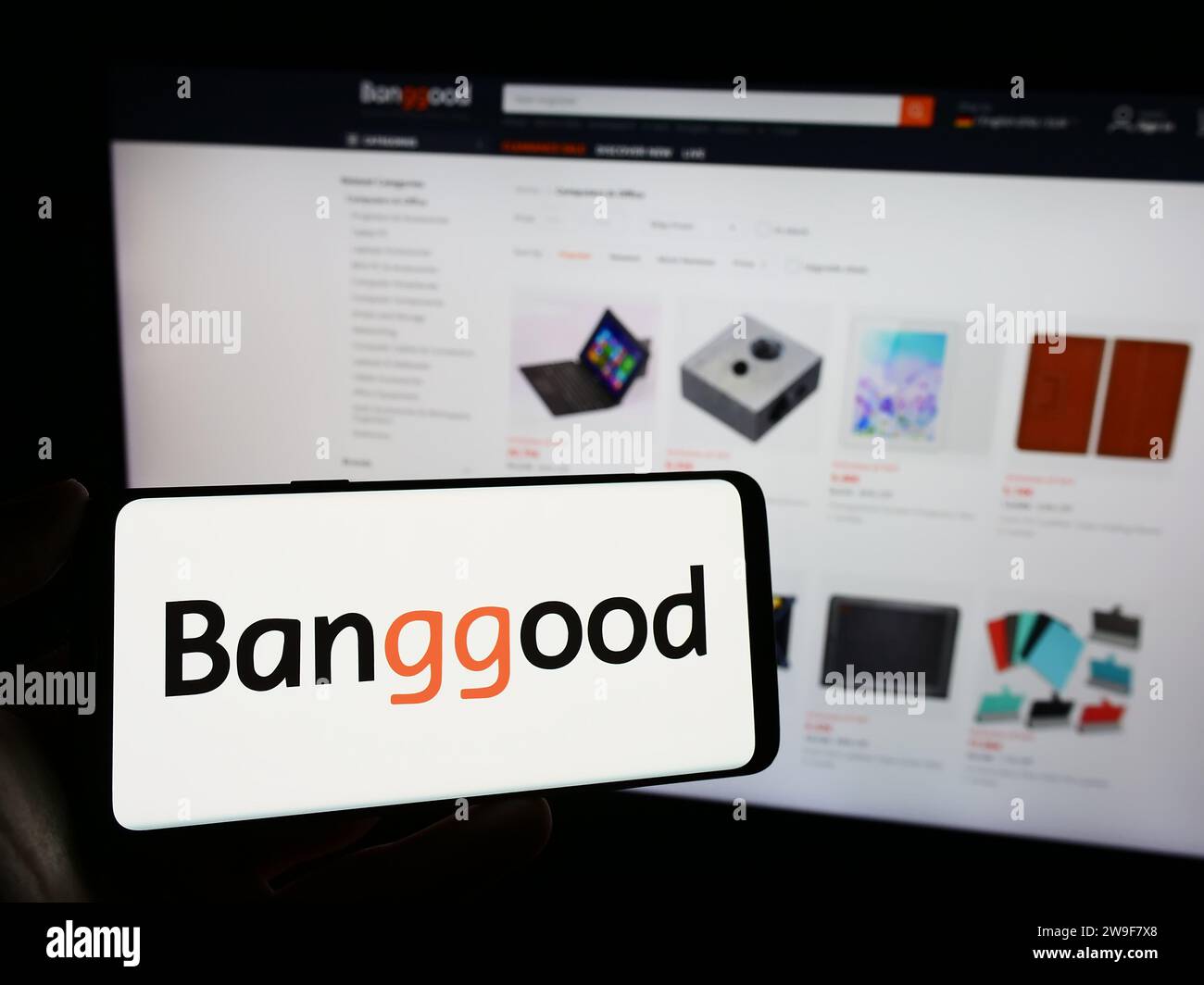 Person, die ein Mobiltelefon mit dem Logo des chinesischen E-Commerce-Unternehmens Banggood Wholesale vor der Business-Webseite hält. Schwerpunkt auf dem Display des Telefons. Stockfoto