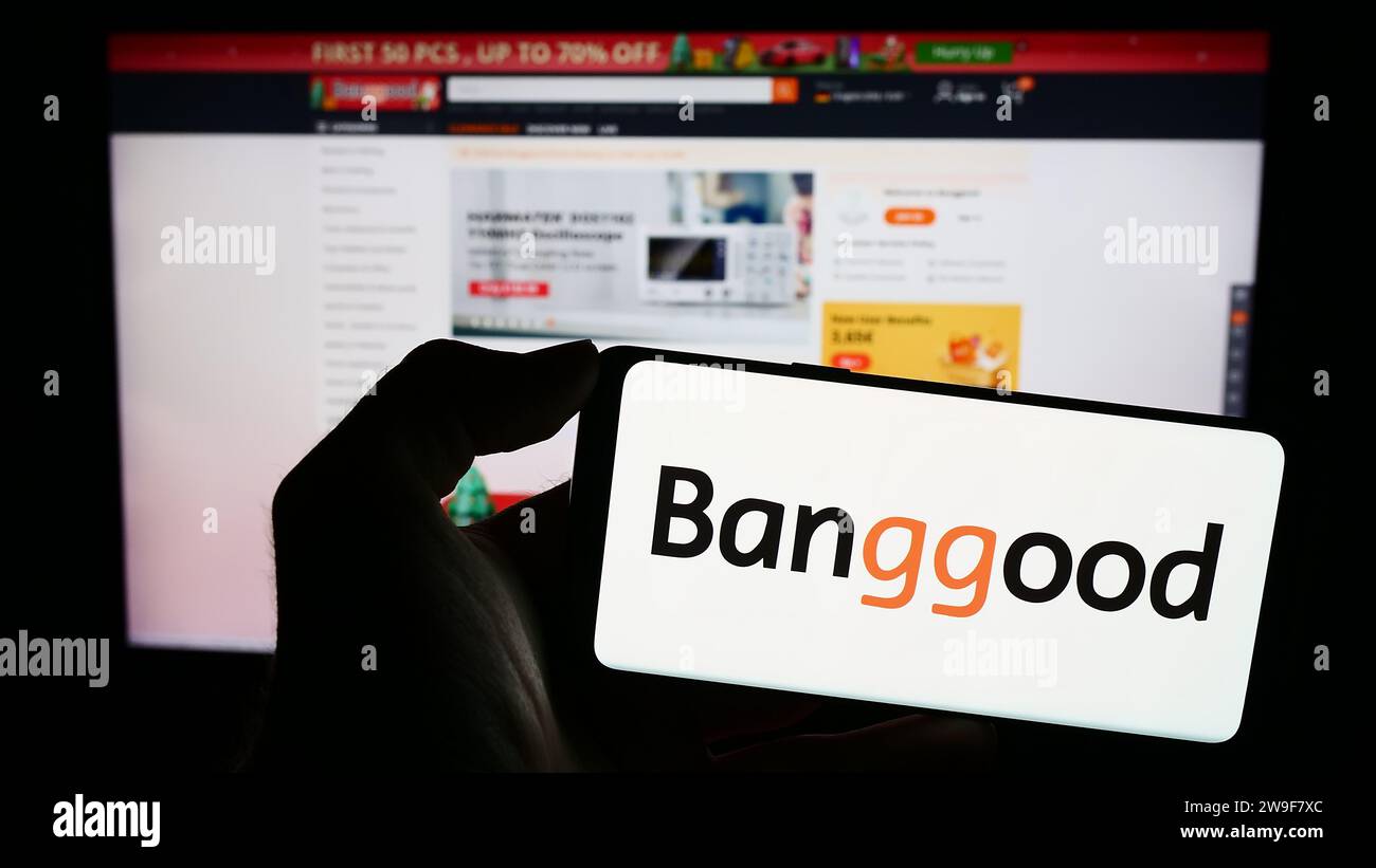Person, die ein Mobiltelefon mit dem Logo des chinesischen E-Commerce-Unternehmens Banggood Wholesale vor der Business-Website hält. Schwerpunkt auf dem Display des Telefons. Stockfoto