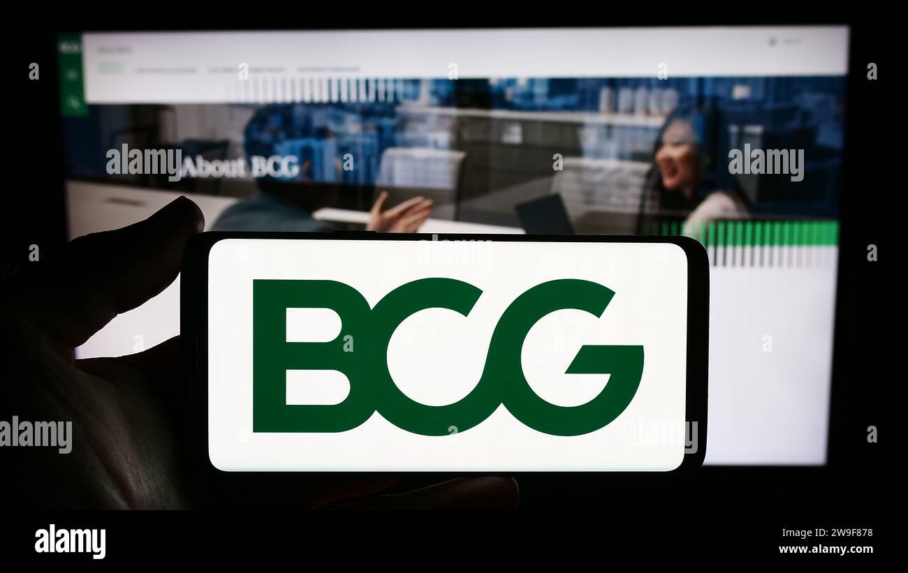 Person mit Smartphone und Logo der US-amerikanischen Firma Boston Consulting Group Inc (BCG) vor der Website. Schwerpunkt auf dem Display des Telefons. Stockfoto