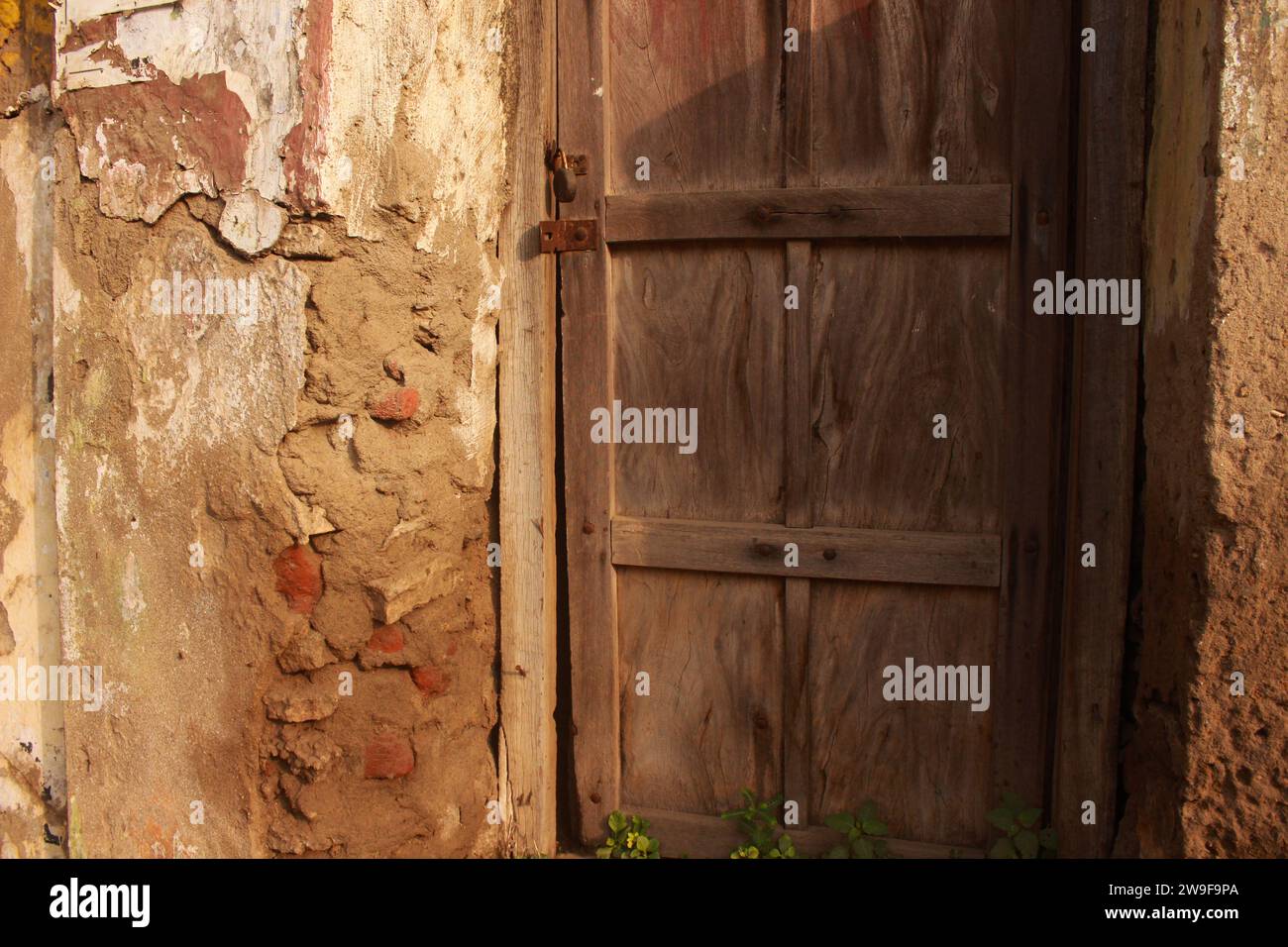 Eine verwitterte Holztür mit abblätternder Farbe ist in eine rustikale Ziegelwand eingefasst Stockfoto