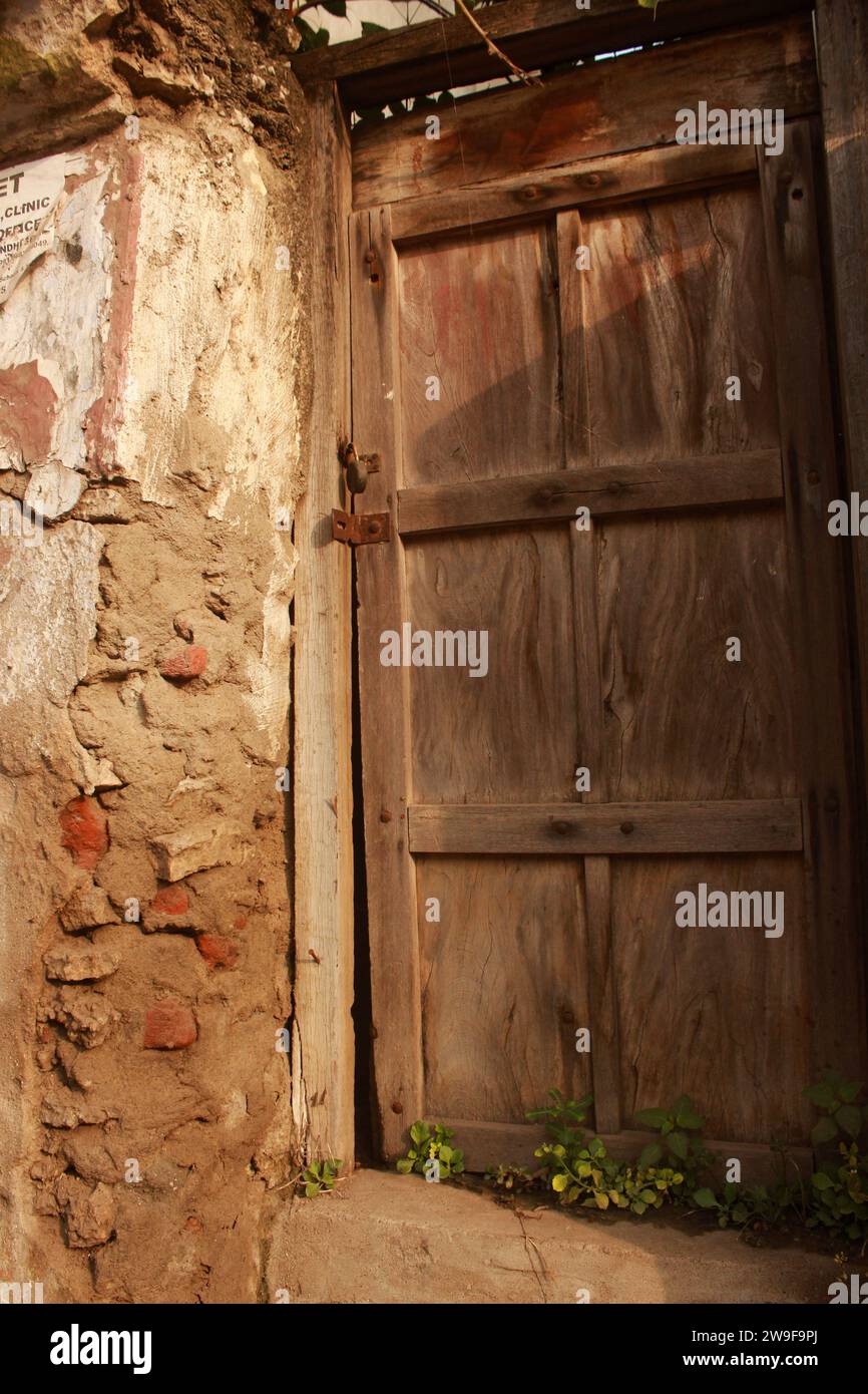 Eine verwitterte Holztür mit abblätternder Farbe ist in eine rustikale Ziegelwand eingefasst Stockfoto
