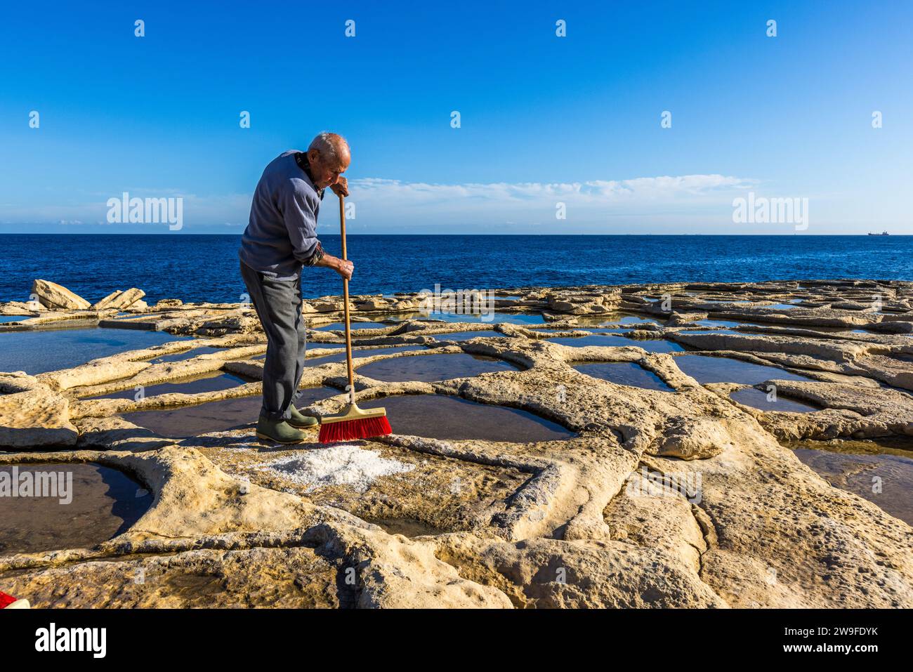 Żaren Darmanin, Salzbauer in Malta, demonstriert die Salzernte in seinen Salinen in Marsaskala. Die Pfannen sind mit Salzwasser gefüllt. Das Mittelmeer hat einen Salzgehalt von 3 Prozent. Darmanin Salinen in der Nähe von Marsascala, Malta Stockfoto