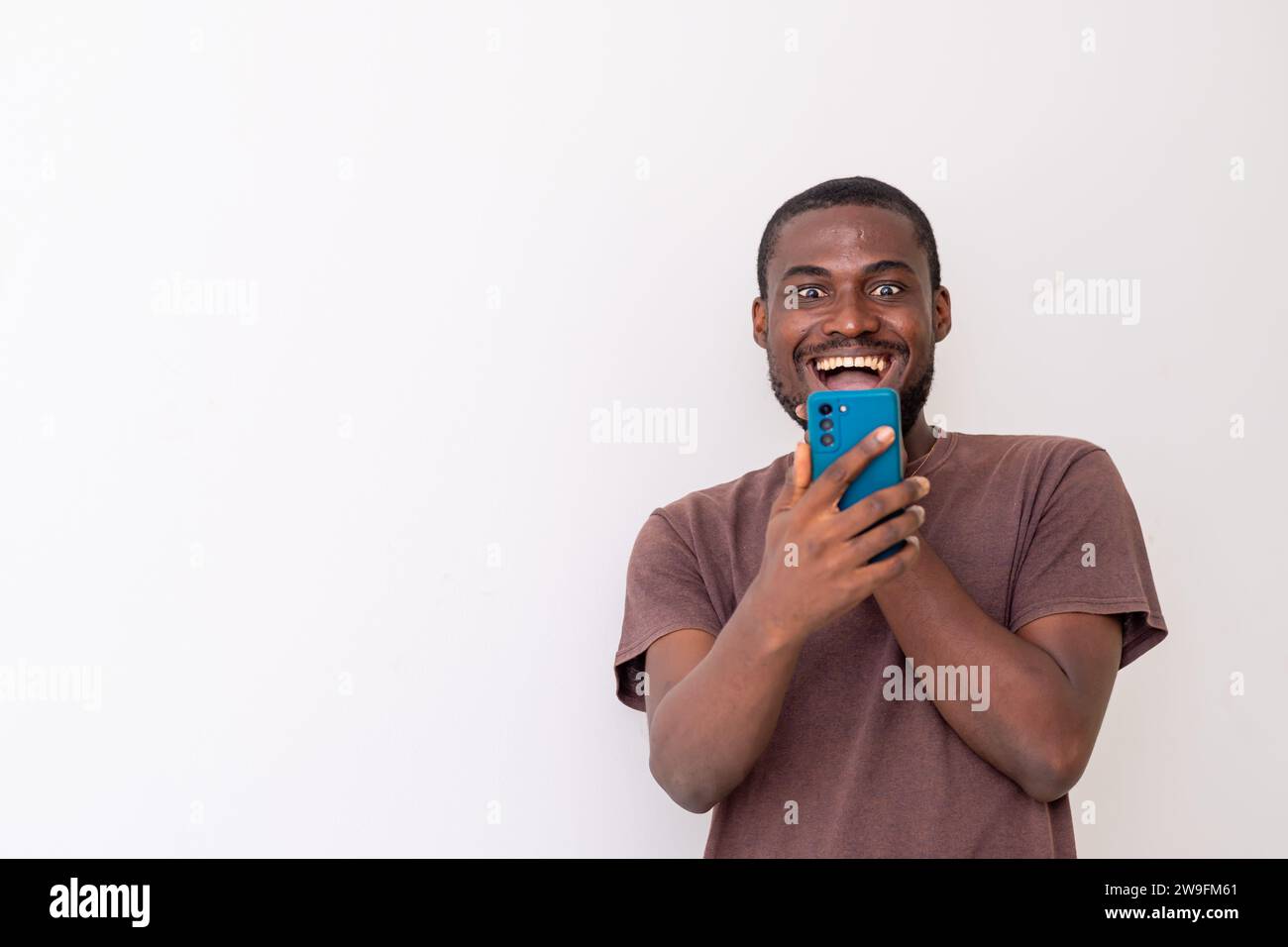 Junger afrikanischer Schwarzer, der auf das Handy blickt, fühlt sich fröhlich an. Technologie, Wireless-Technologie Stockfoto