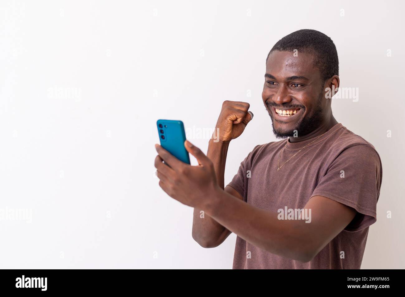 Überglücklich afrikanischer schwarzer Mann, der sich auf das Handy freut, gute Nachrichten zu lesen. Afrikanischer Mann mit Smartphone, um Sportwetten online zu wetten. T Stockfoto