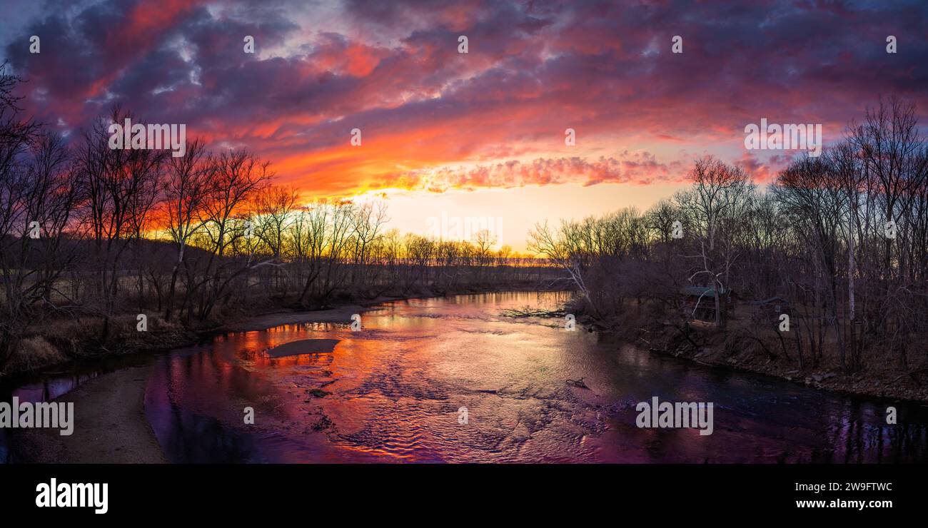 Ein lebhafter und farbenfroher Sonnenuntergang über dem flachen Wasser des White River in der Nähe von Seymour, IN. Viele warme Farben; Orange und Gelb, blaue Schatten Stockfoto