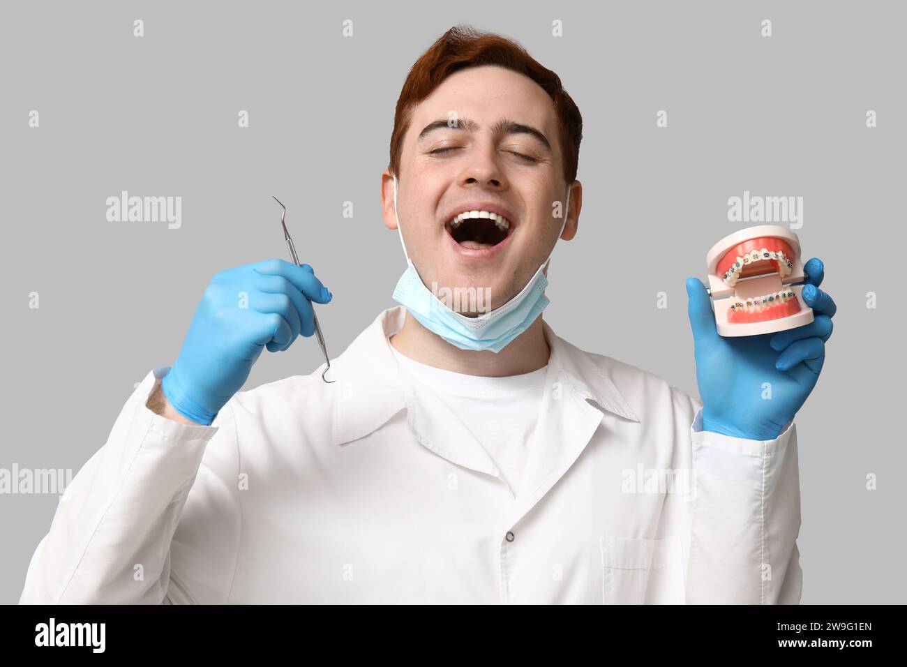 Männlicher Zahnarzt mit Zahnforscher und Kiefermodell auf grauem Hintergrund. Weltzahnarzttag Stockfoto